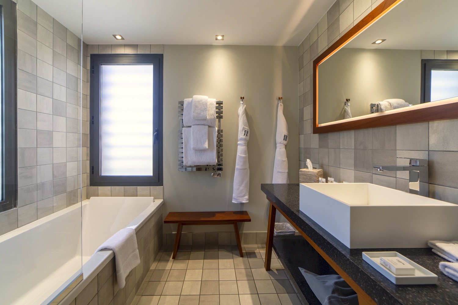 Salle de bain moderne en bois et pierre avec baignoire, vasque rectangulaire et grand miroir design rétroéclairé.