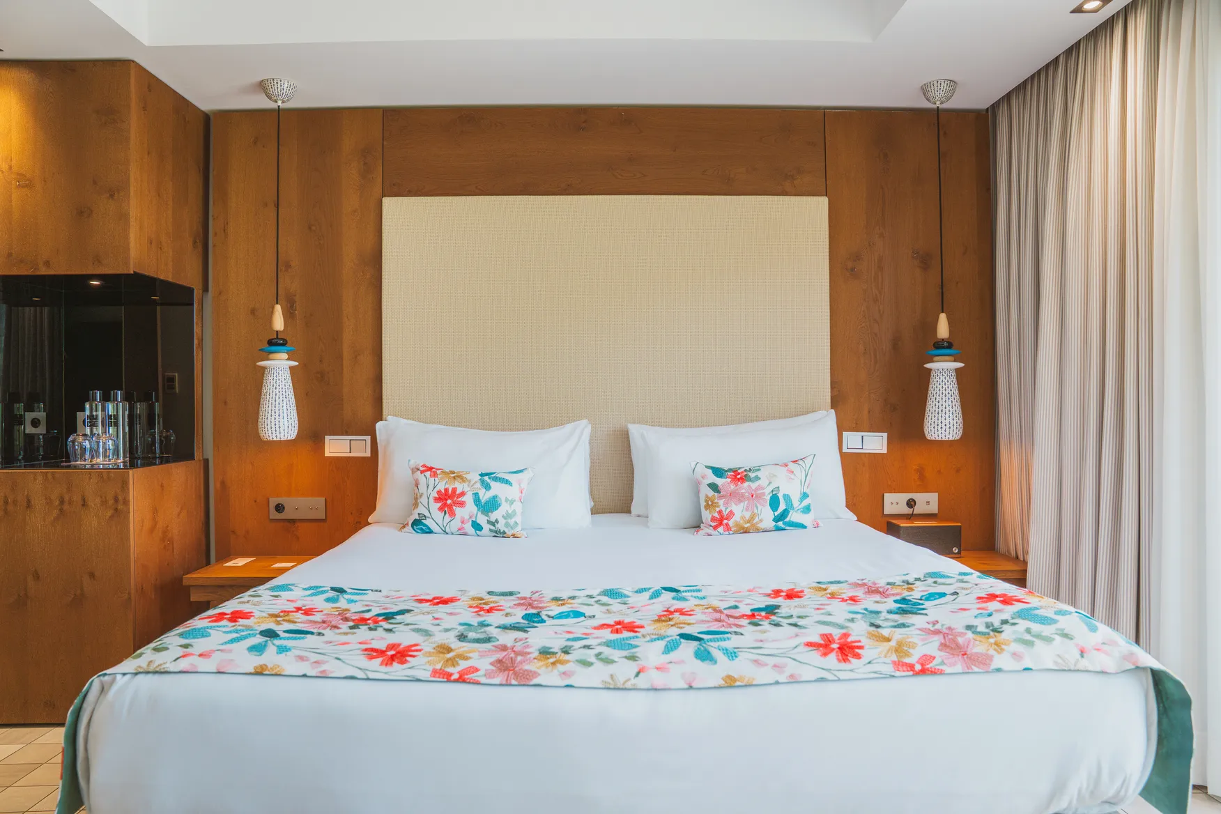 Design intérieur chaleureux d'une chambre Deluxe avec mobilier en chêne clair et décoration textile florale élégante.