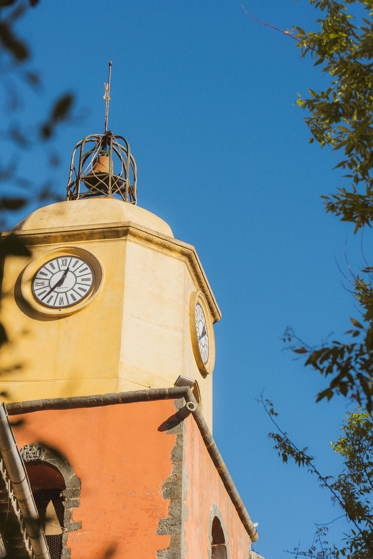 Photo du clocher de l'église Notre-Dame-de-l'Assomption à Saint-Tropez, avec ses couleurs ocre et sienne sous un ciel bleu azur.