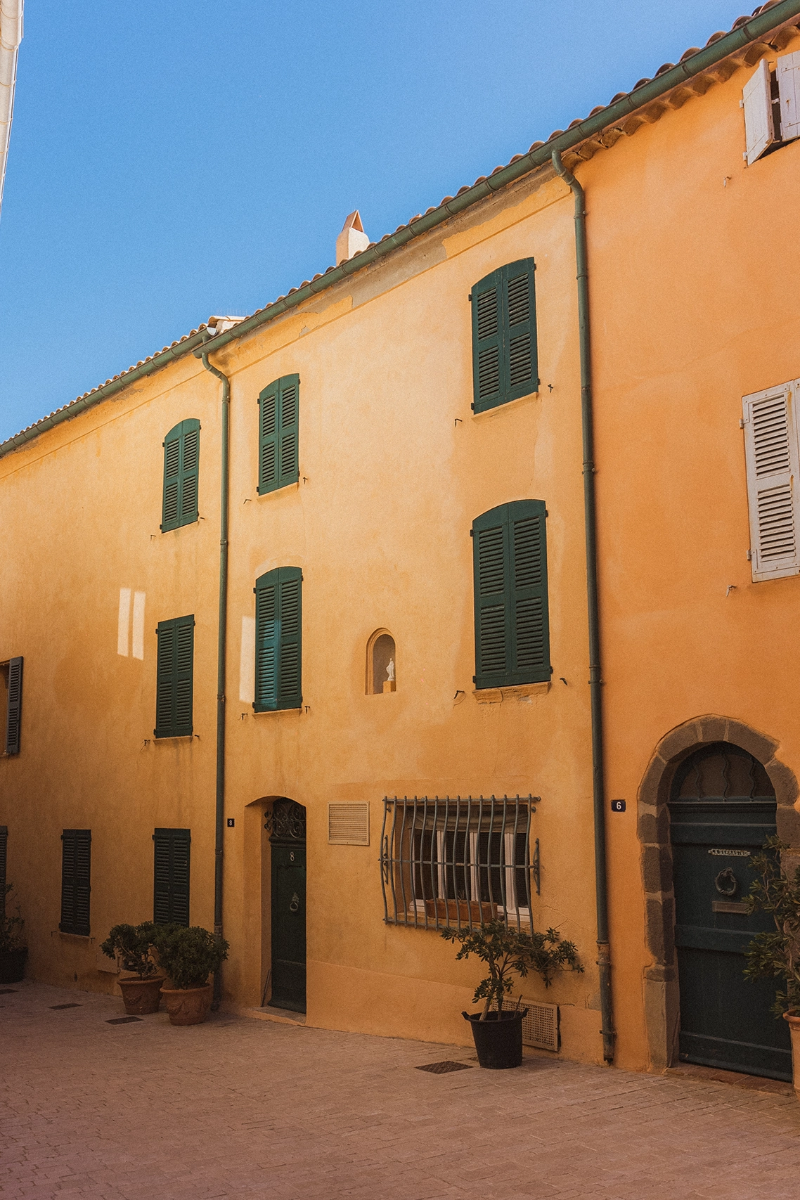 Façade traditionnelle de Saint-Tropez aux murs jaunes et volets verts sous le ciel bleu de la Côte d'Azur.