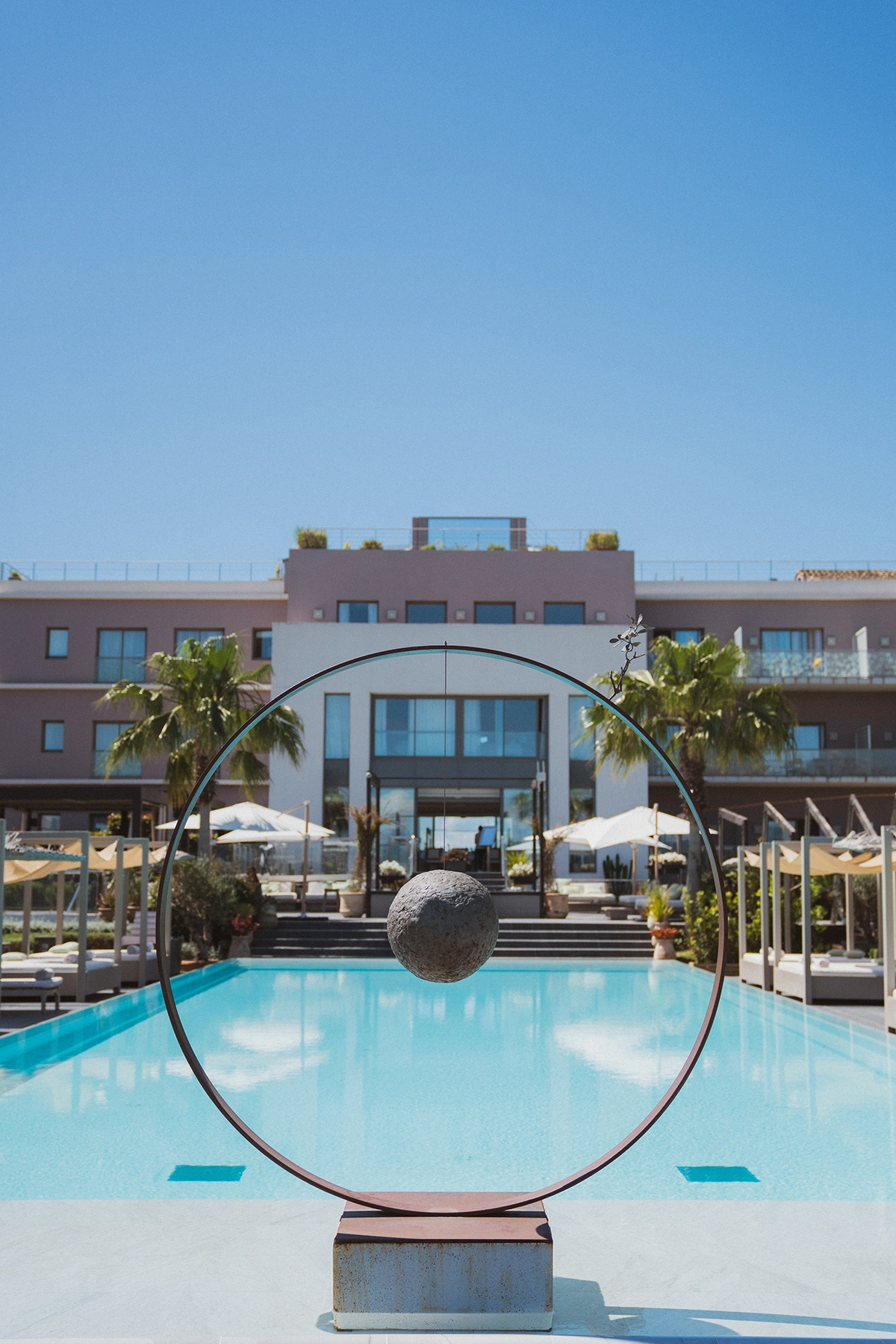 Bassin principal de l'Hôtel Kube Saint-Tropez avec sculpture artistique circulaire et vue sur l'architecture design de l'établissement.