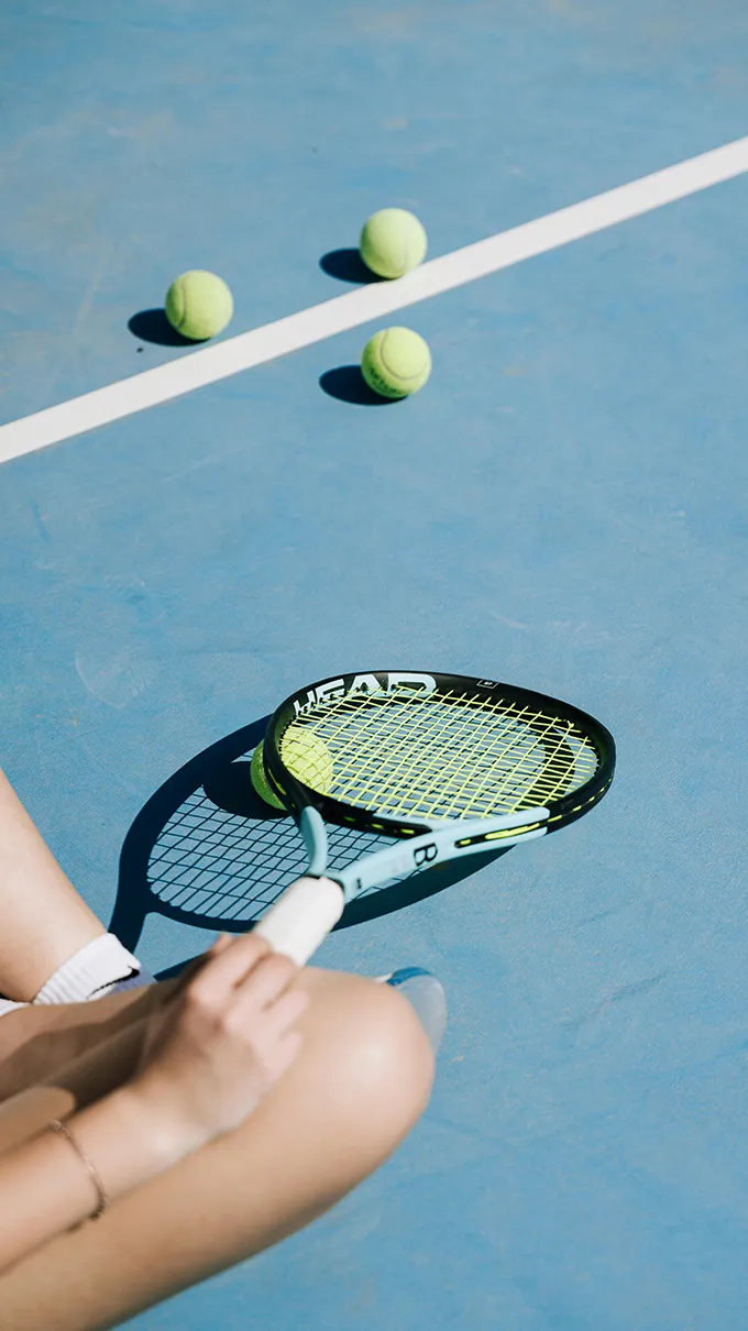Raquette de tennis et balles jaunes sur un court bleu ensoleillé lors d'une partie à Saint-Tropez.