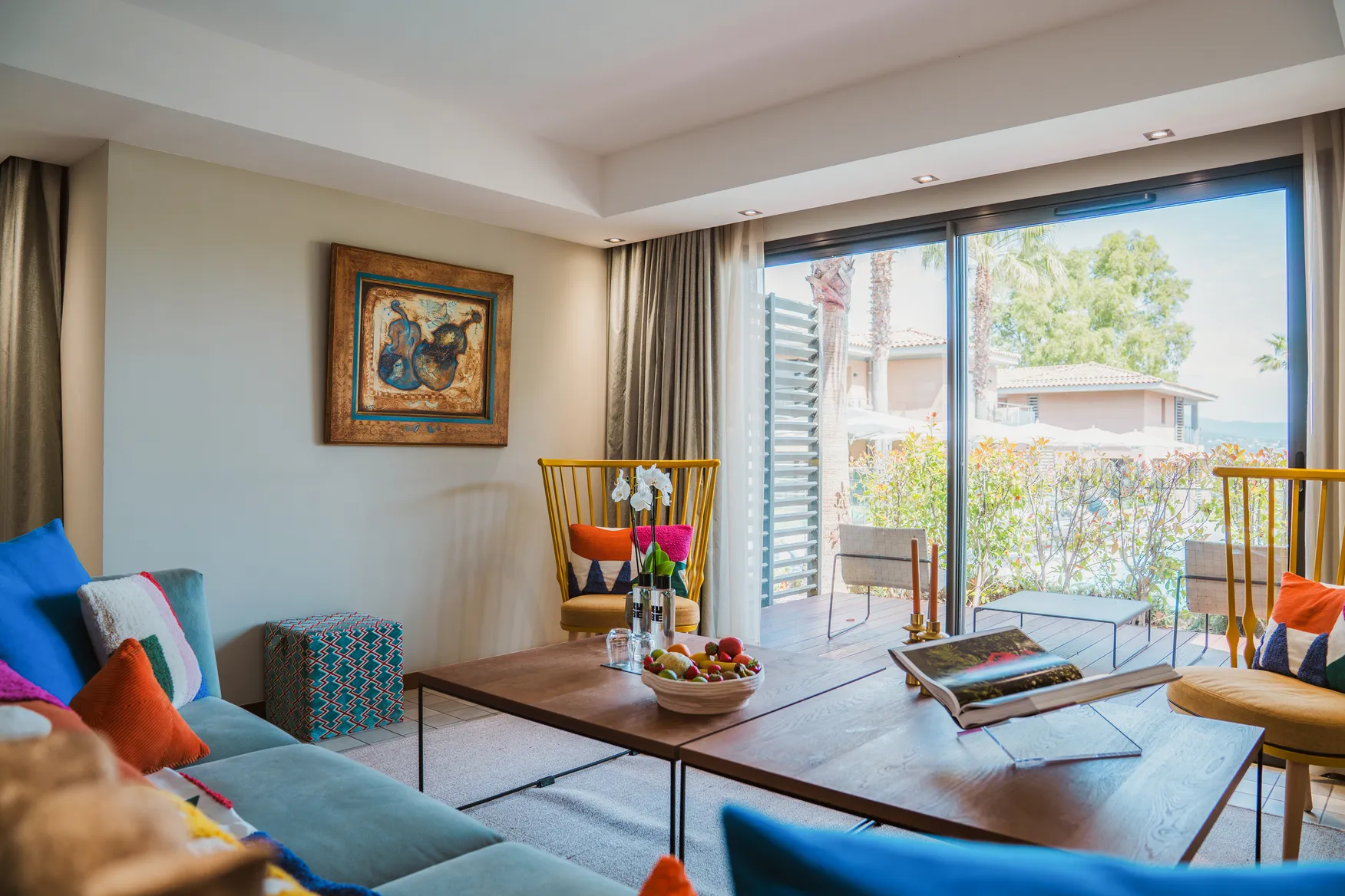 Intérieur de villa de luxe à Saint-Tropez : salon design lumineux s'ouvrant sur une grande terrasse en bois ombragée et un jardin méditerranéen.