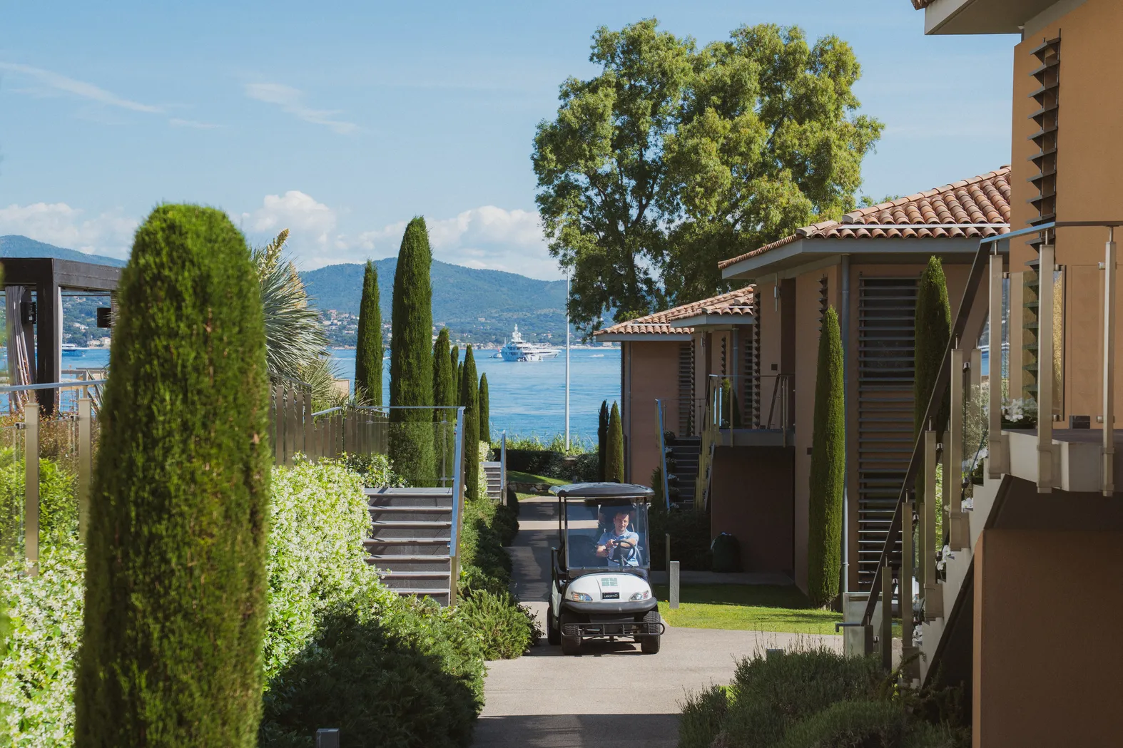 Domaine hôtelier privé à Saint-Tropez avec service de voiturette, allée bordée de cyprès offrant une vue sur le Golfe de Saint-Tropez.