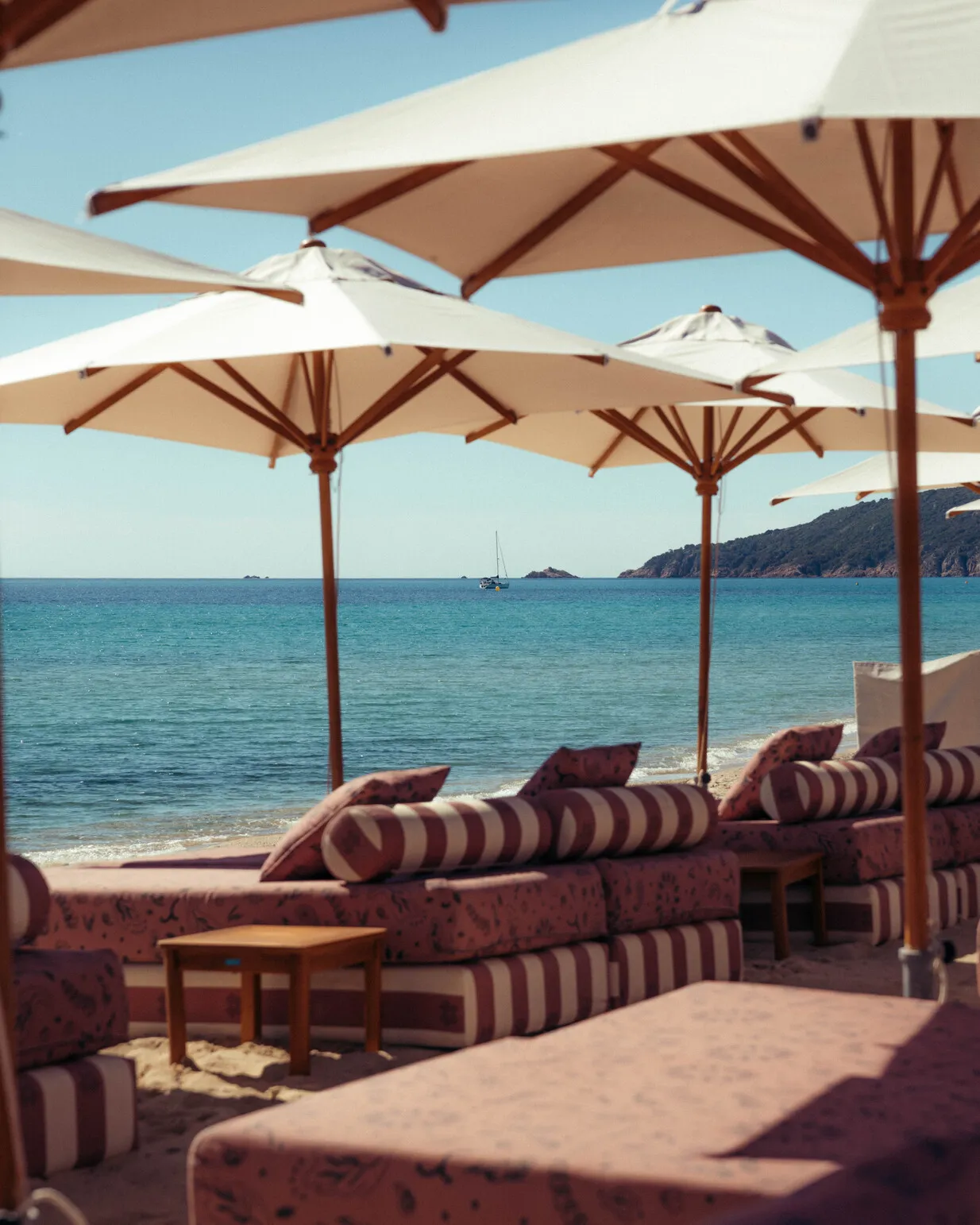 Espace lounge chic sur le sable de la Plage Cybelle à Ramatuelle, avec banquettes rayées, tables en bois et parasols face à la mer azur.