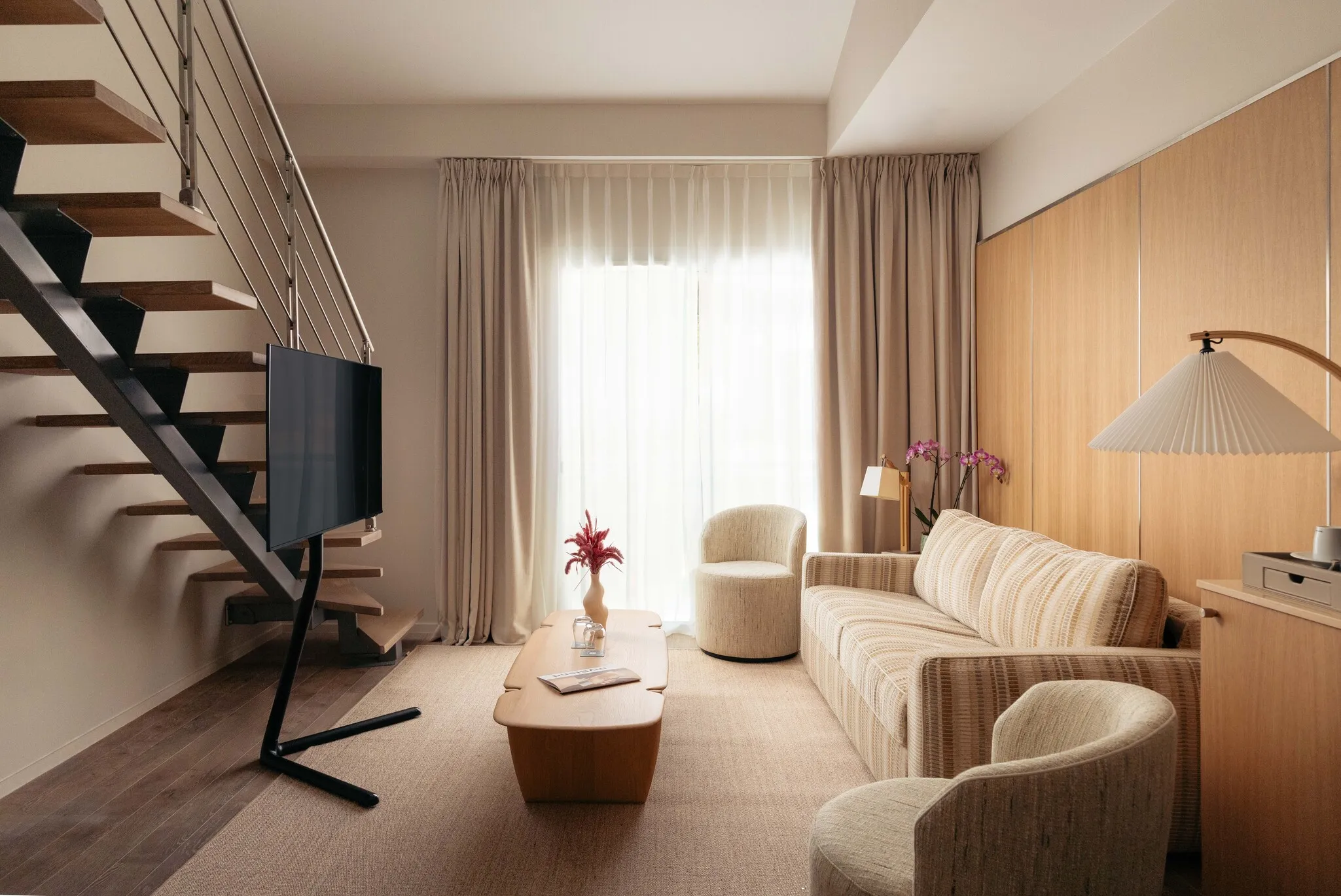 Salon lumineux en rez-de-chaussée de la suite Junior Natural en duplex avec canapé confortable et escalier.