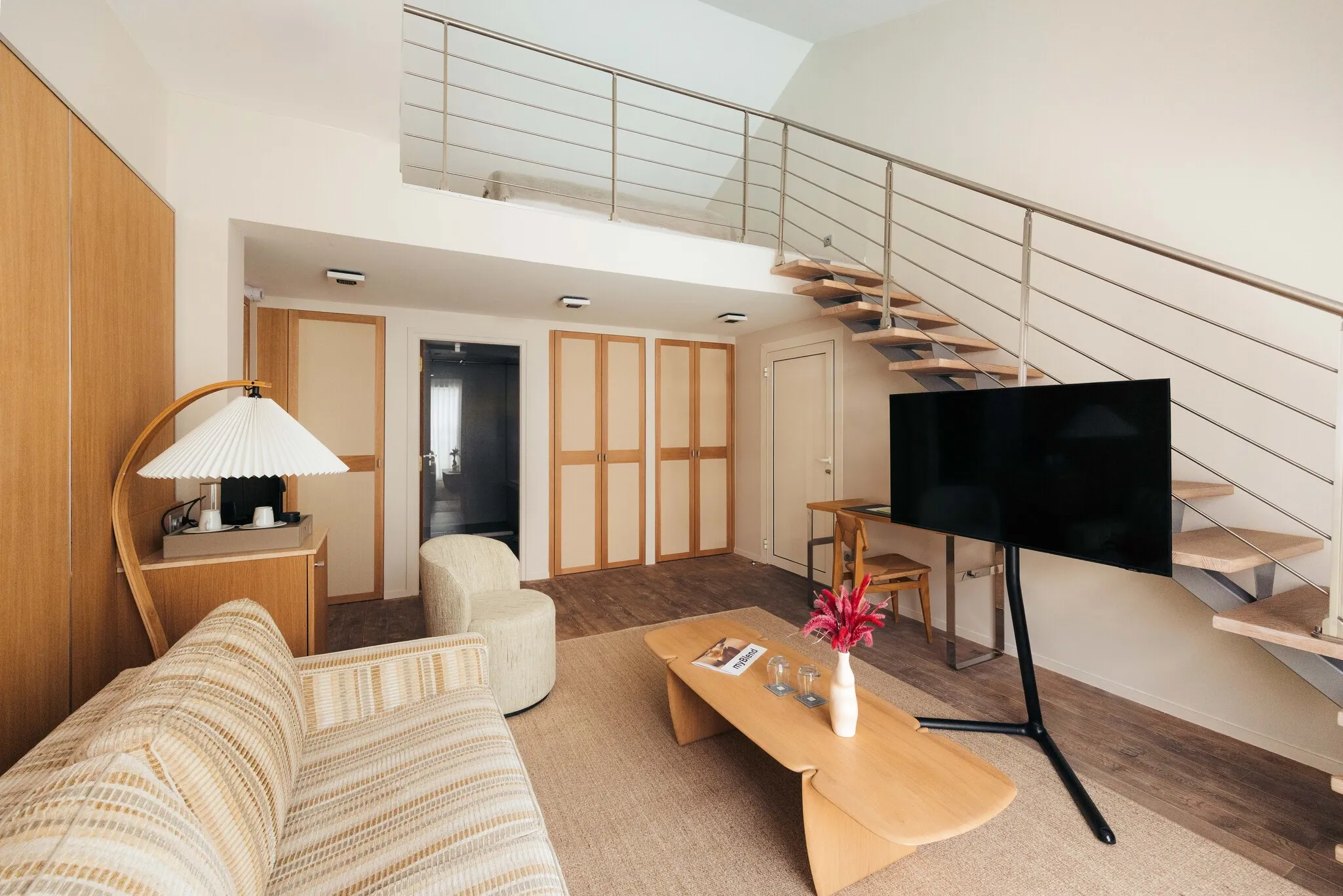 Espace de vie esprit loft de la chambre Junior Natural avec canapé, table basse en bois et vue sur la mezzanine.