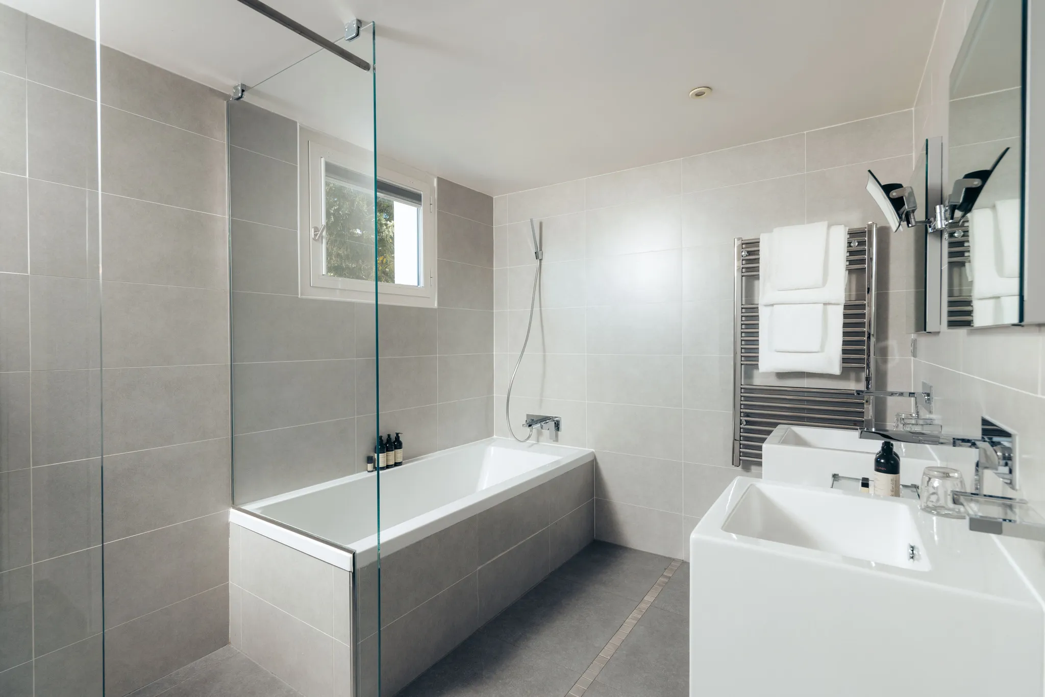 Salle de bain contemporaine revêtue de carrelage gris avec baignoire et vasque blanche, suite Junior Natural.