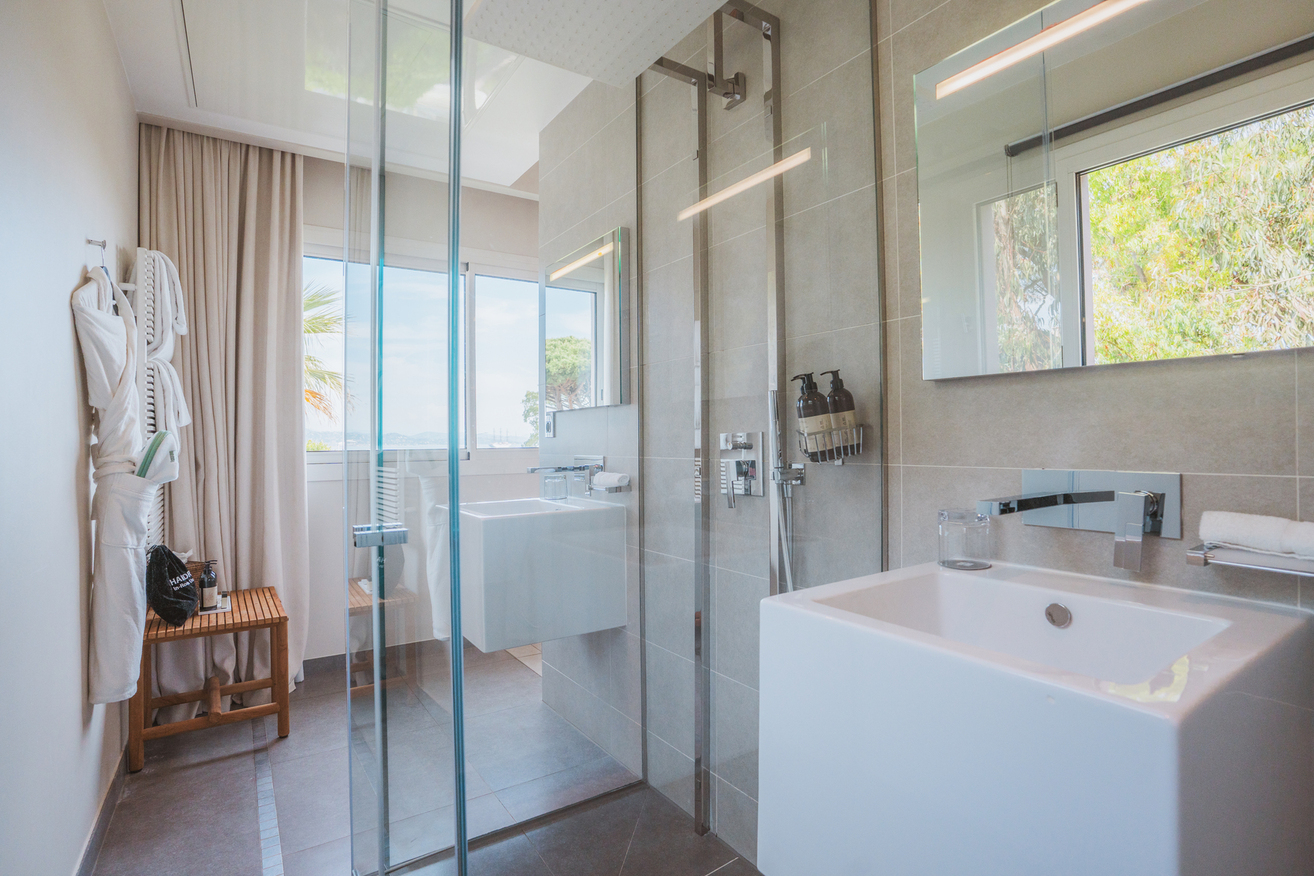 Salle de bain moderne et lumineuse de la chambre Natural avec douche à paroi vitrée et vasque blanche.