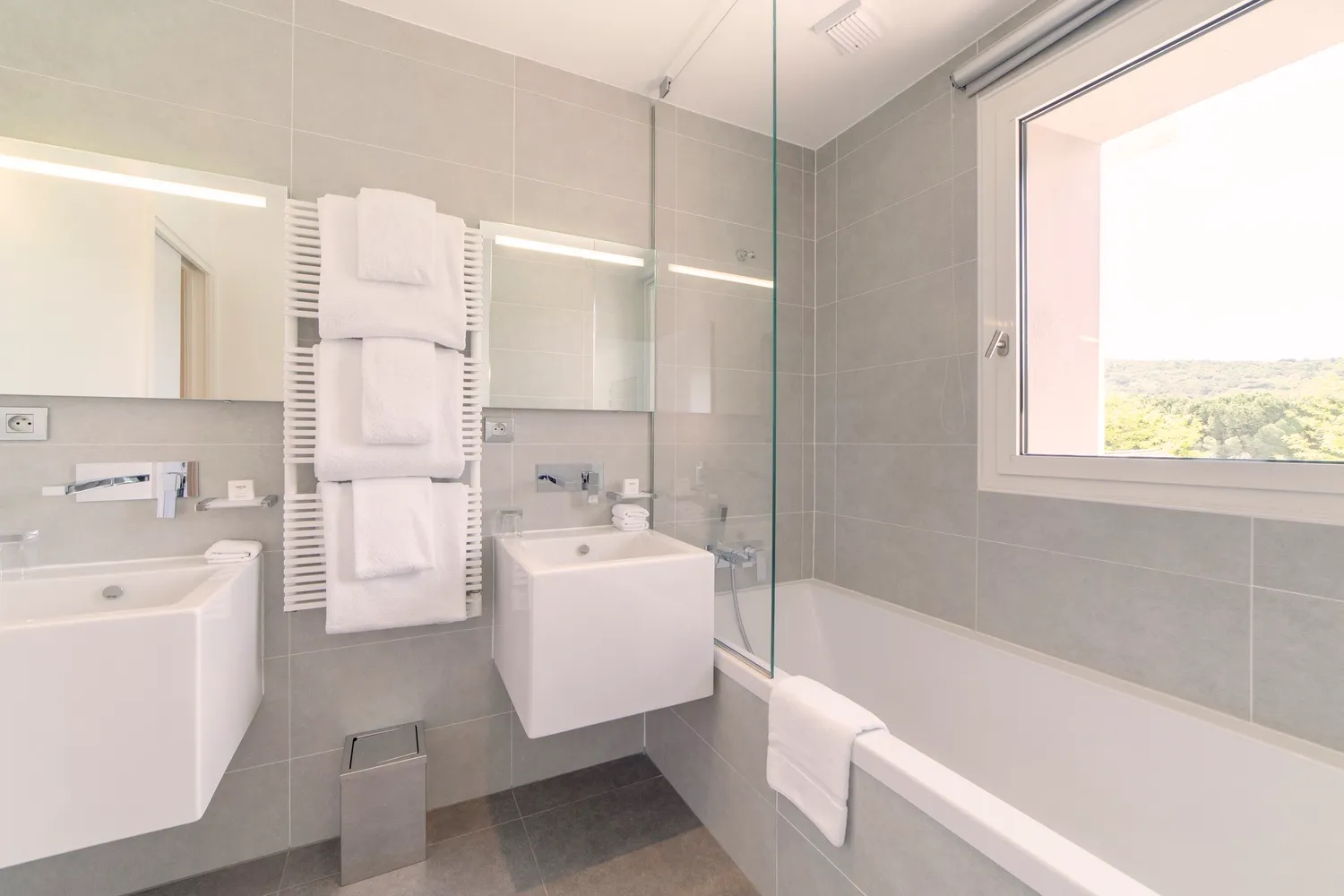 Salle de bain lumineuse avec baignoire et grand miroir, associée à la chambre Prestige Natural.