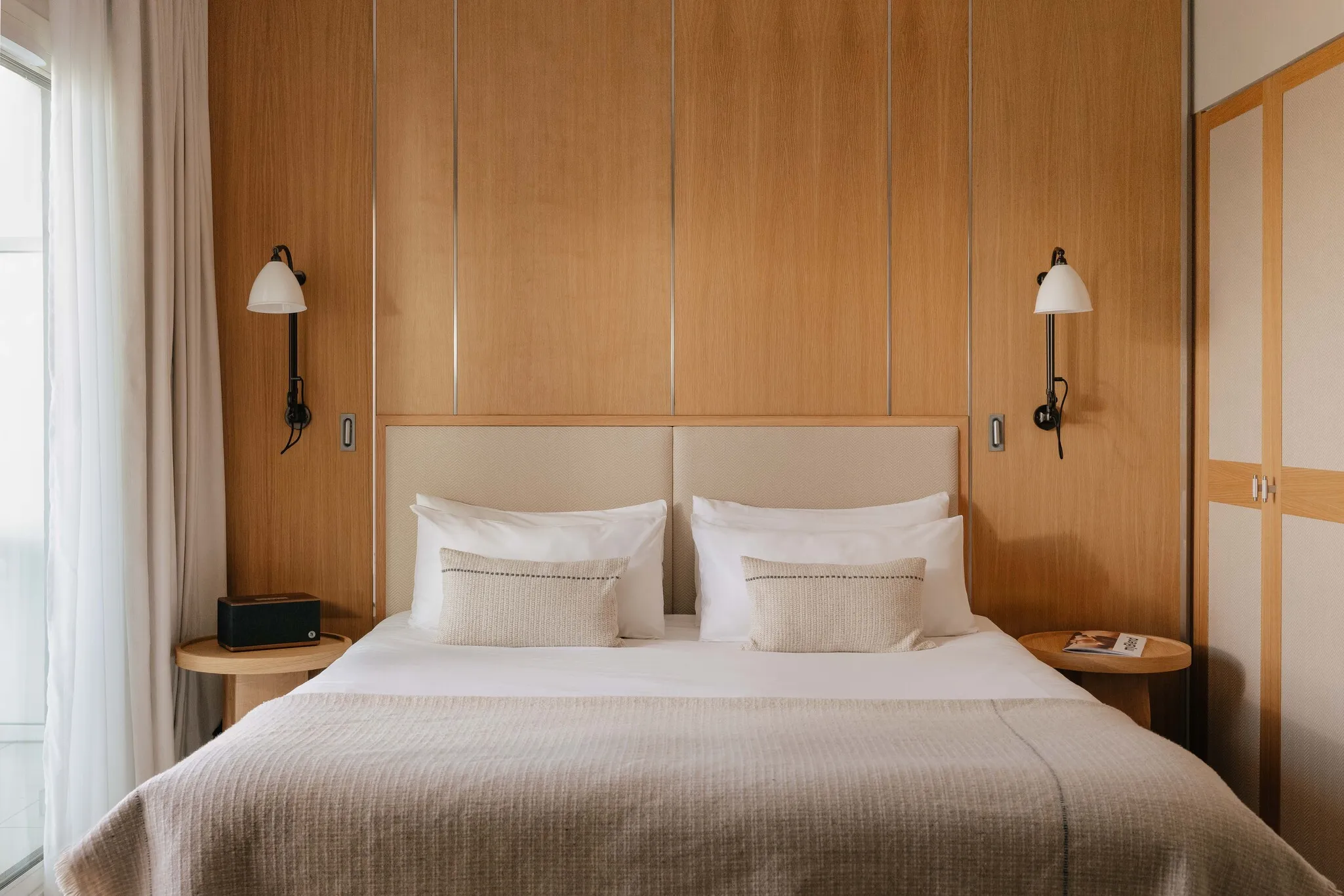 Lit king size centré devant un mur en bois clair chaleureux avec lampes de chevet dans la suite Prestige Natural Sea.