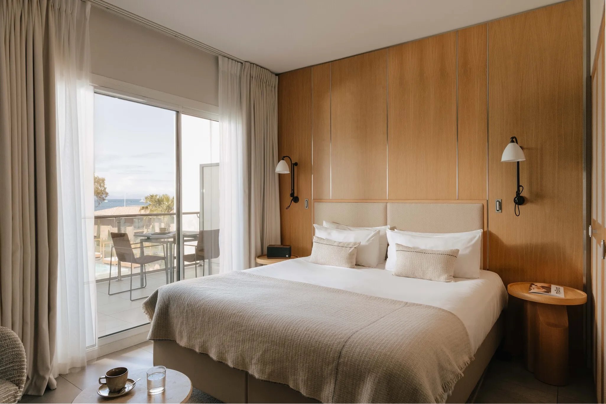 Grande suite Prestige Natural Sea avec lit double, habillage mural en bois et baie vitrée ouvrant sur un balcon.