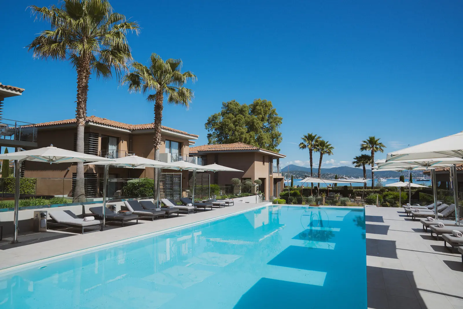 Piscine du Kube Saint-Tropez bordée de transats et de parasols, le golfe en arrière-plan