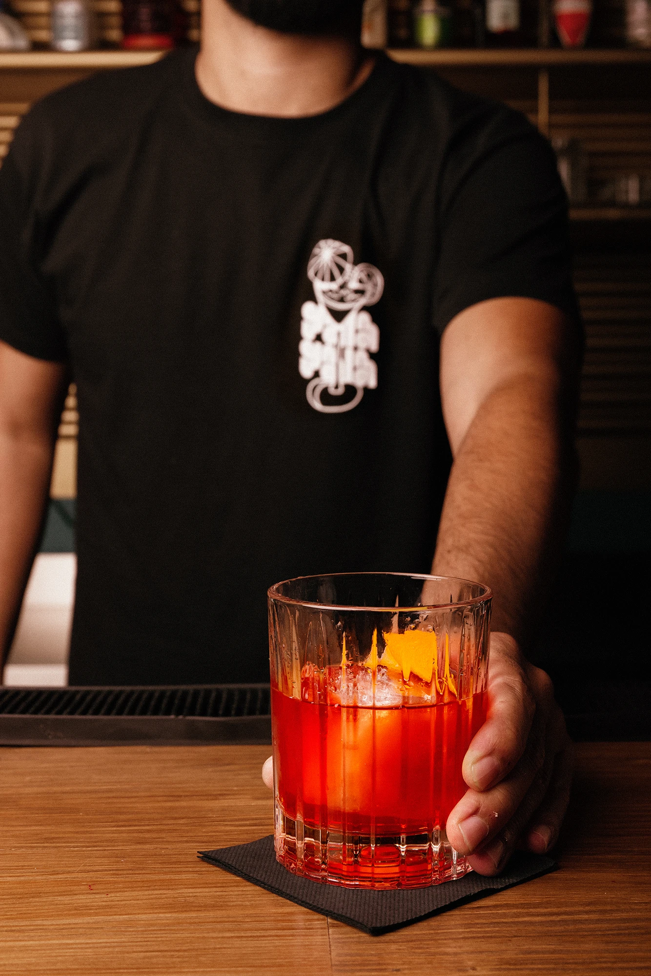 Bartender wearing Gala Gala branded black t-shirt holding a cocktail

