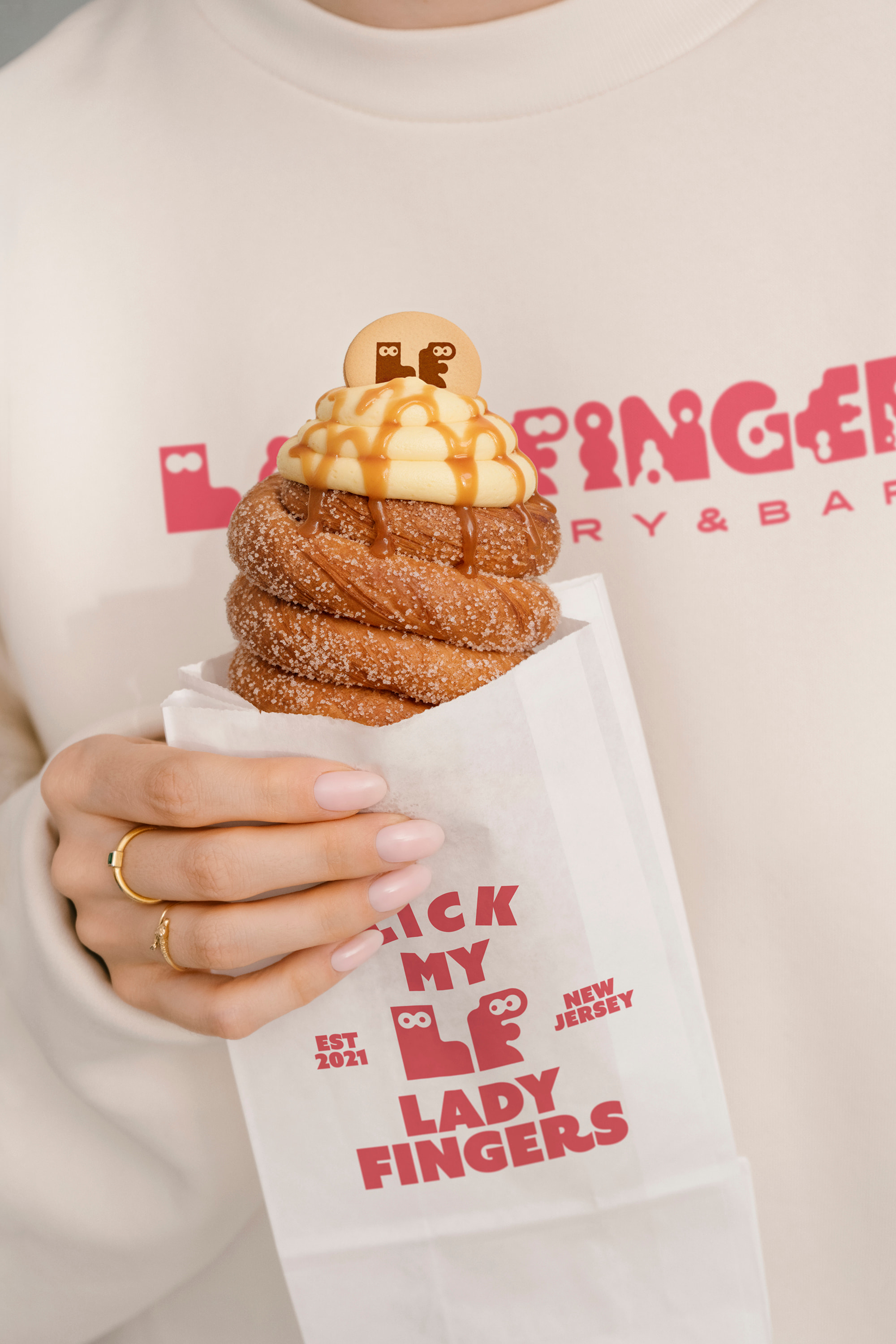 Hand holding a Ladyfingers branded paper bag with a pastry

