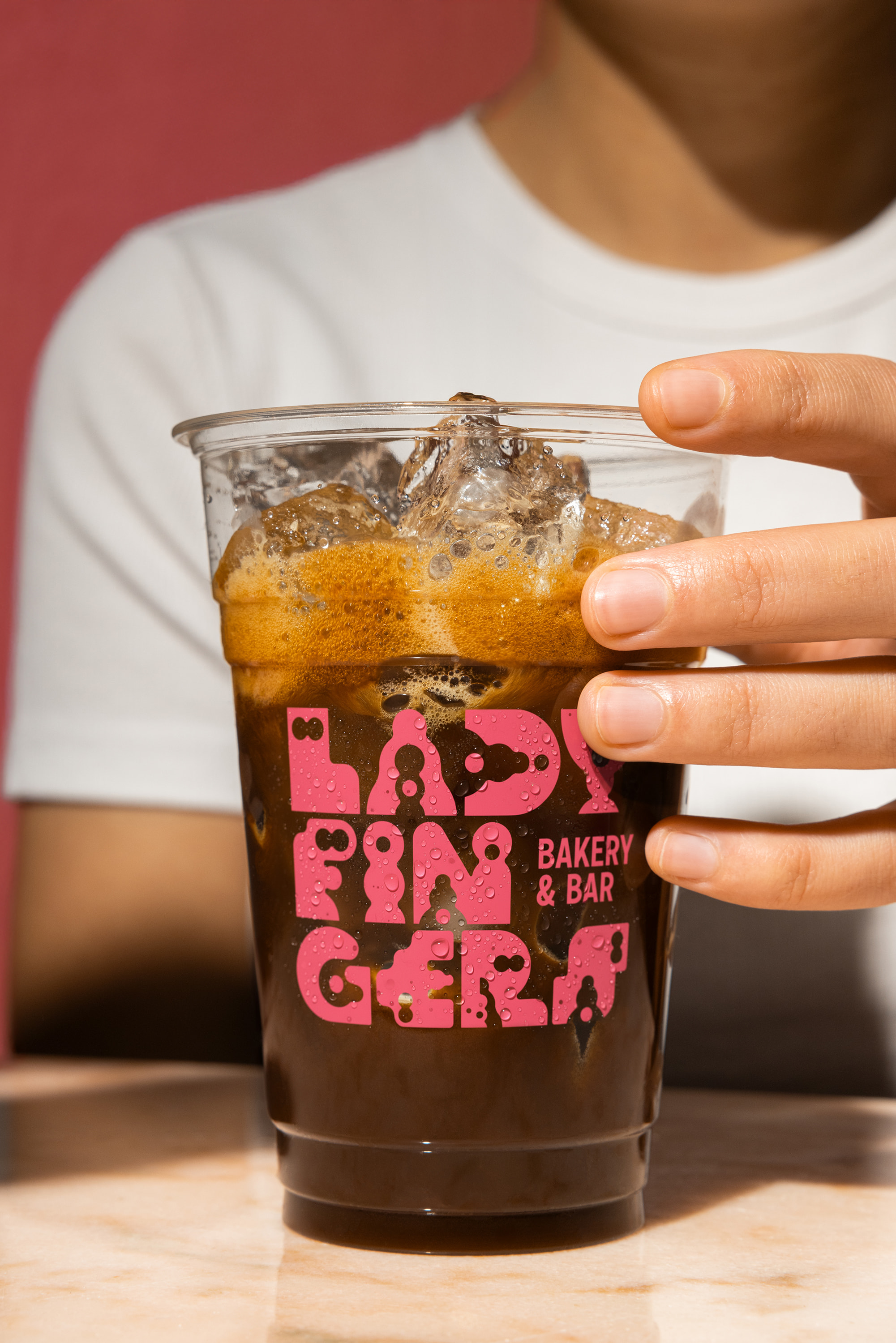 Hand holding a Ladyfingers branded plastic cup with iced coffee
