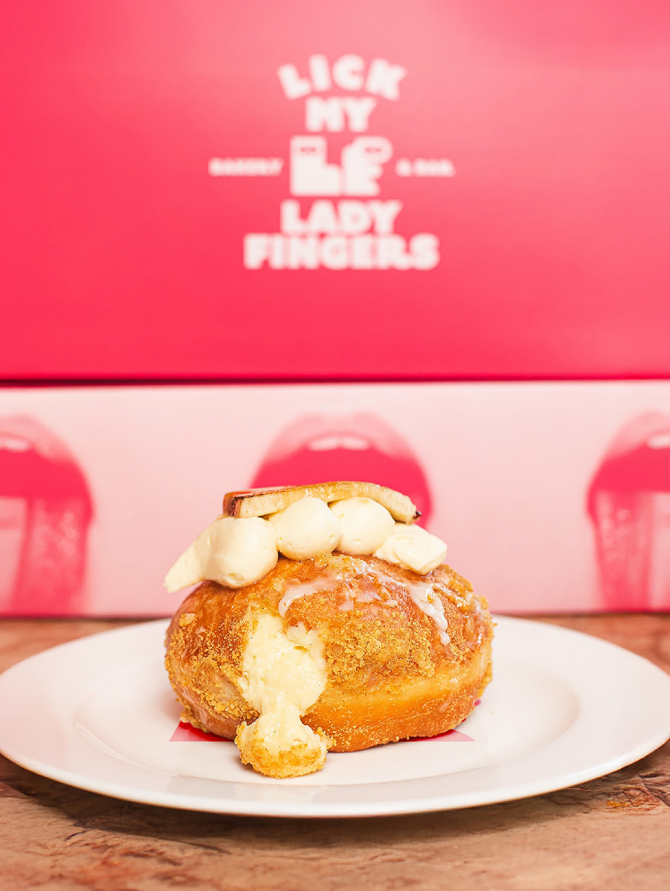 Ladyfingers branded donut with cream filling on a plate against pink background

