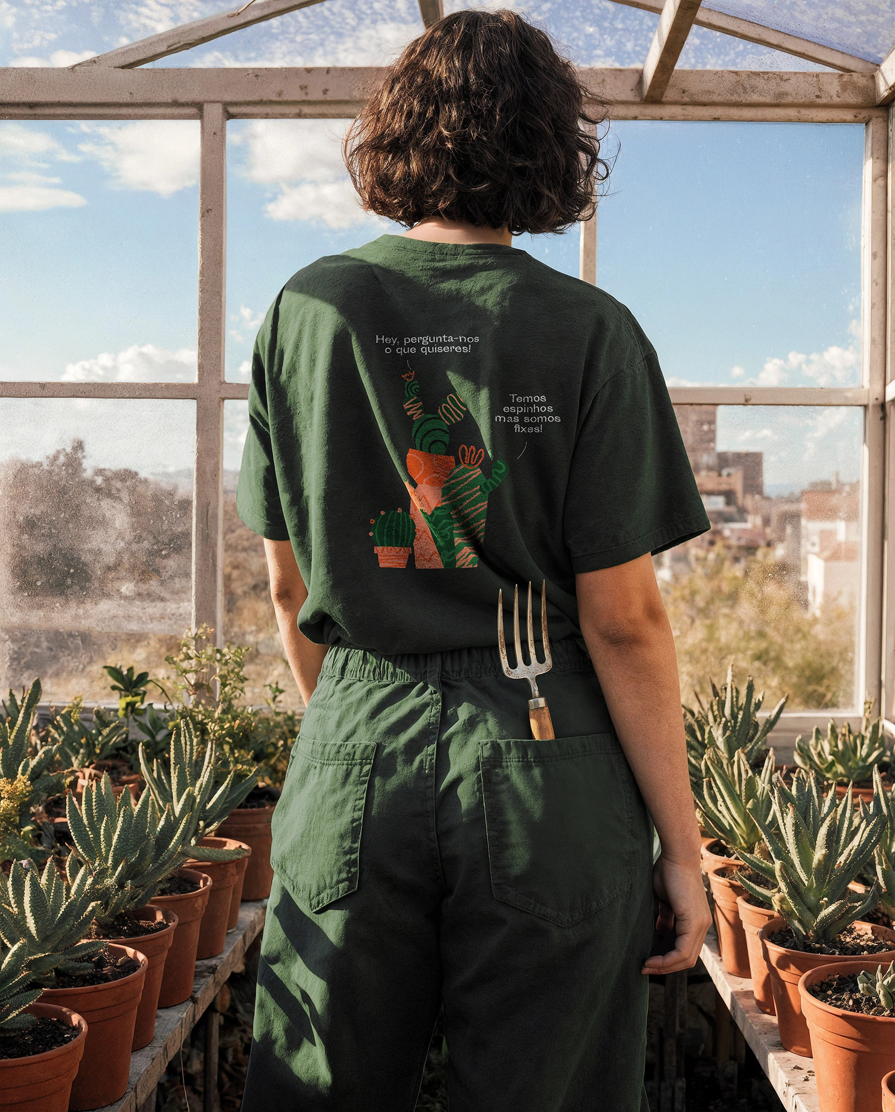 Person wearing Maria Bicuda branded green t-shirt with cactus illustration in a greenhouse