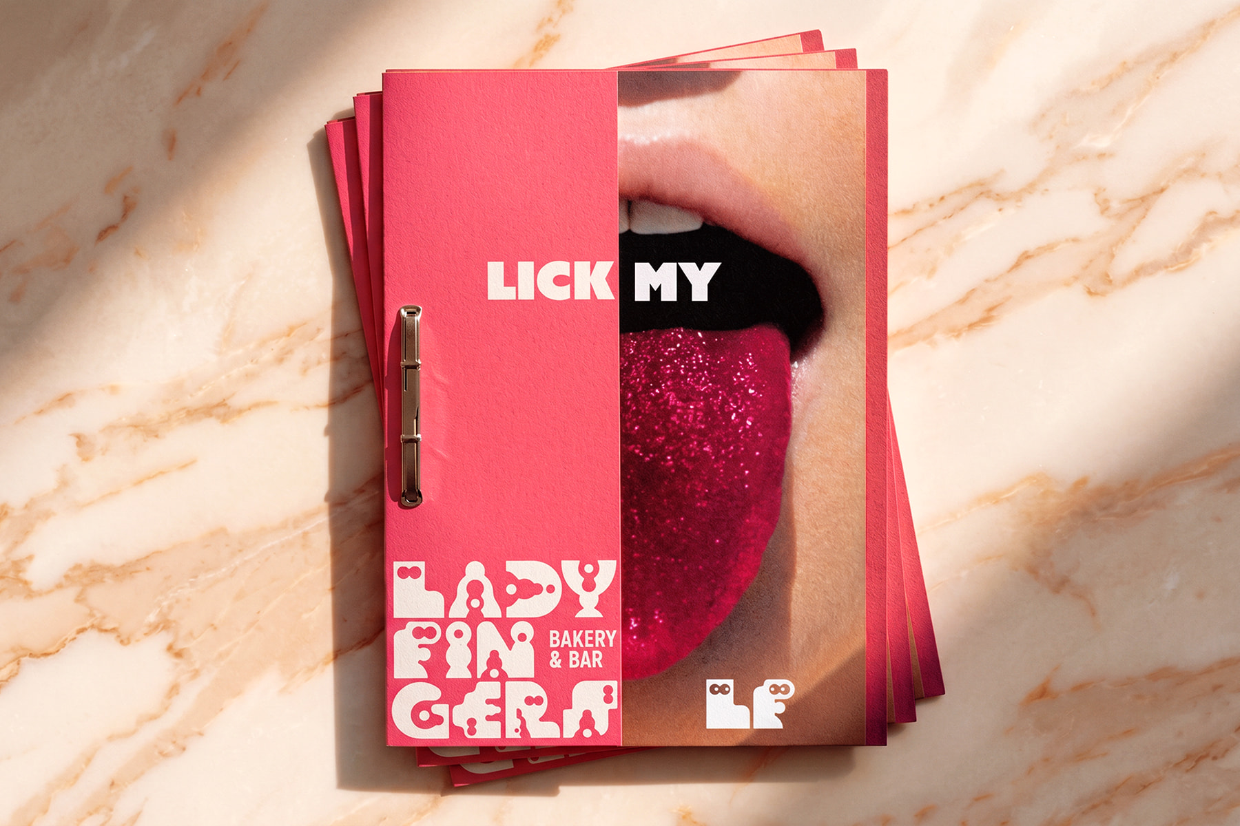 Ladyfingers Bakery and Bar menu covers stacked on marble surface with halftone mouth illustration
