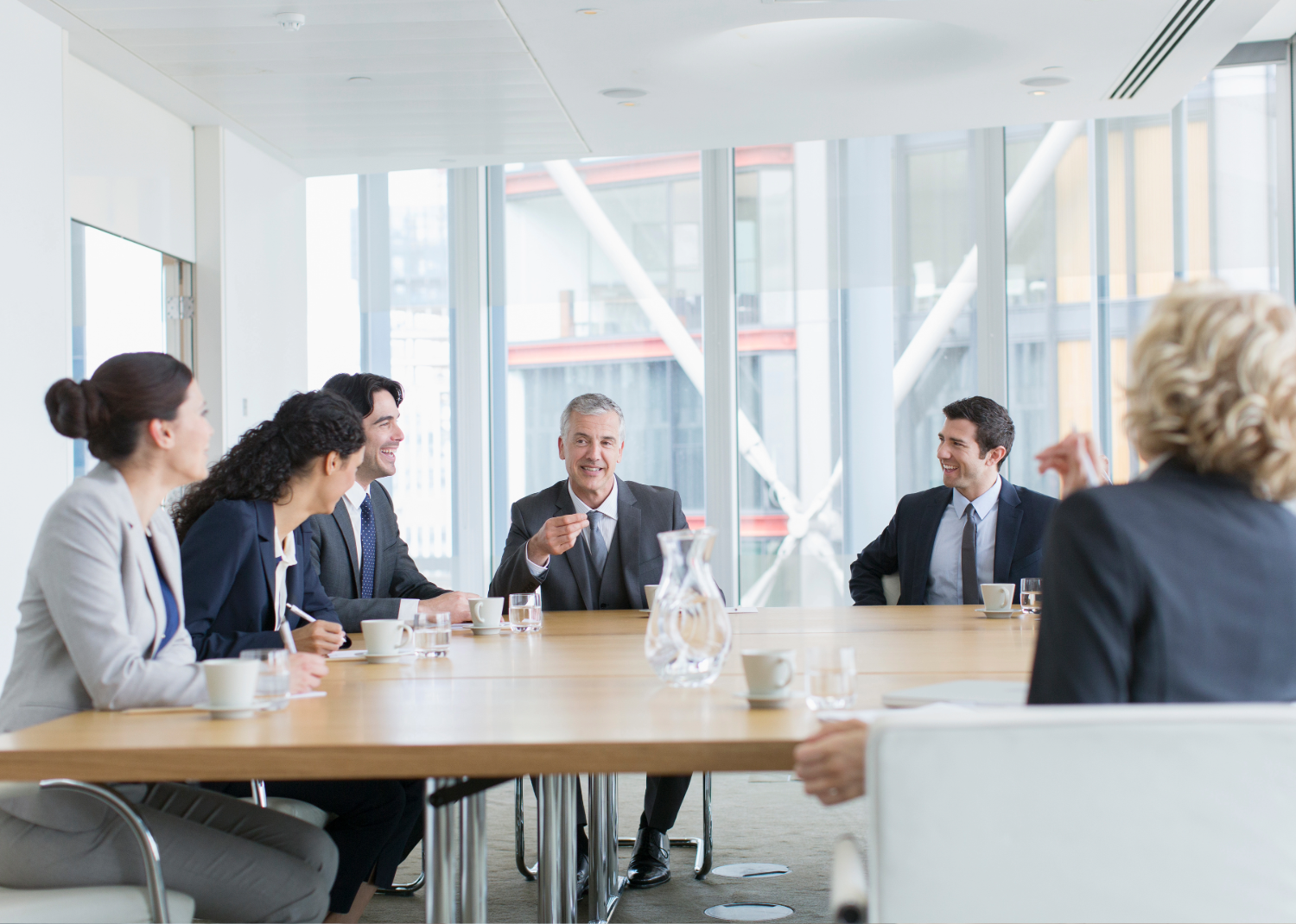 Business team in suits sitting at a conference table having a meeting in a glass office.