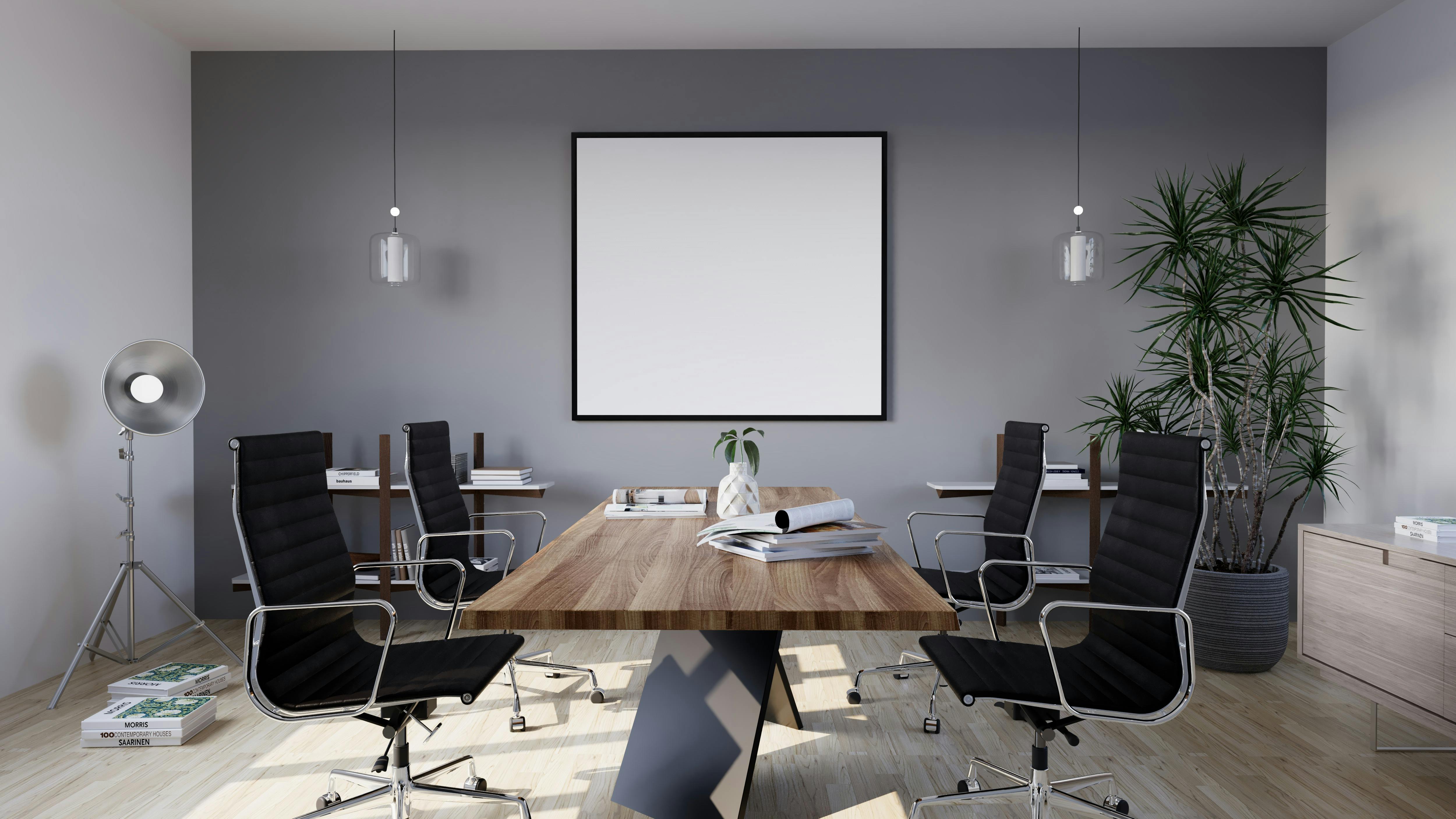 Modern conference room with wooden table, black chairs, a large plant, and a blank wall frame.
