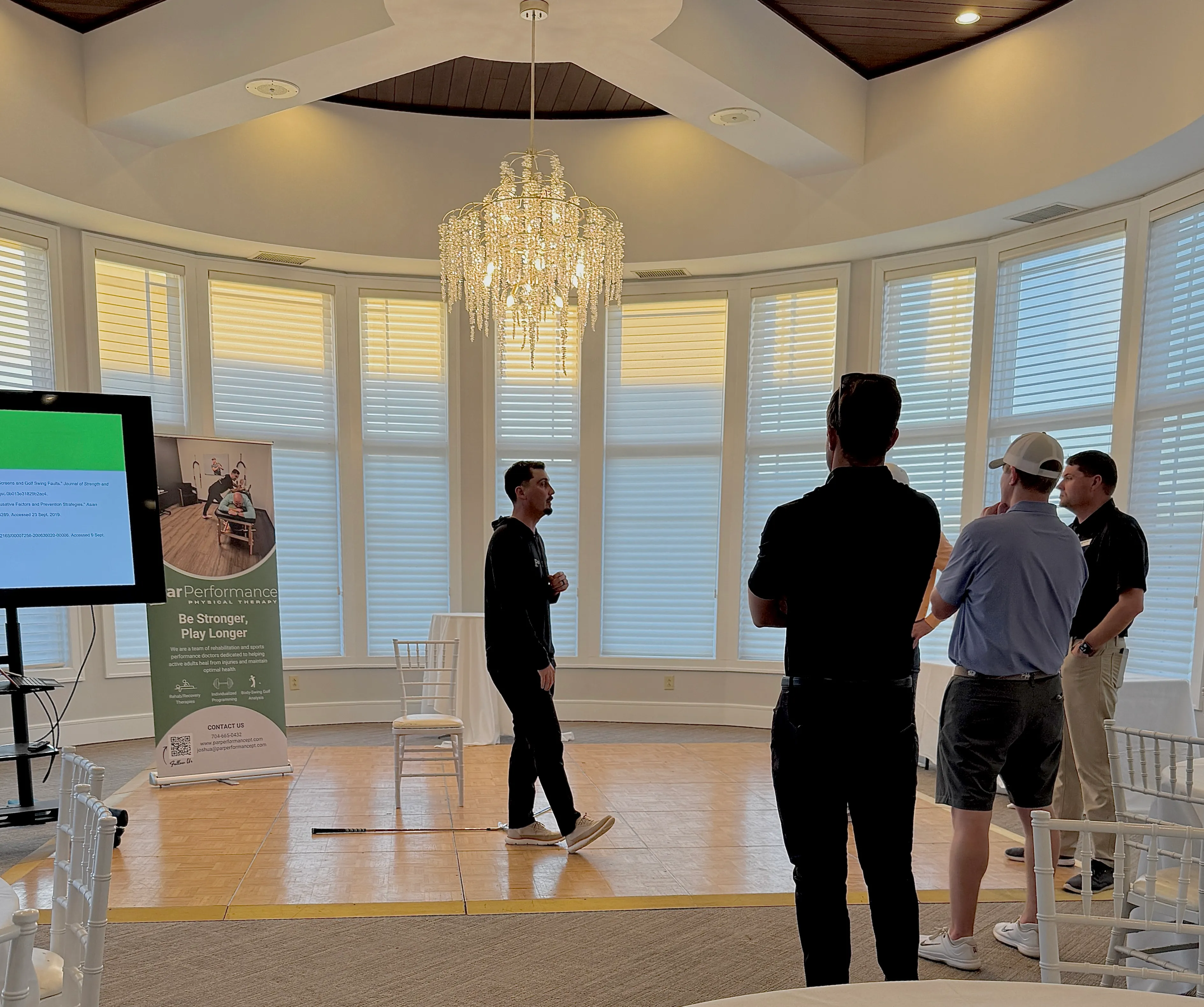 Man giving a presentation to a group of three men in a bright room with large windows and a chandelier.