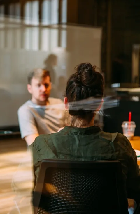 Two people in conversation in an office, seen through a glass window with reflections.