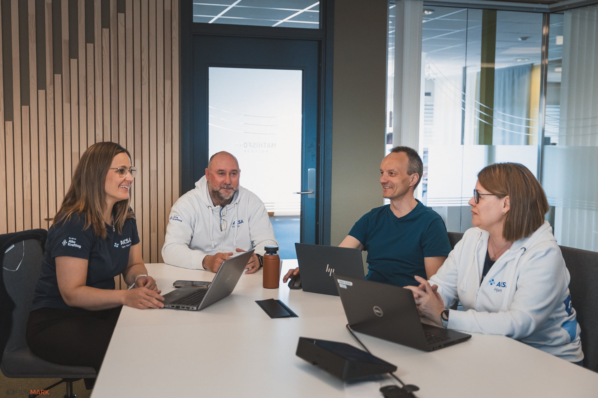 Fire personer i et møte på kontor med laptopper og smilende ansikter.