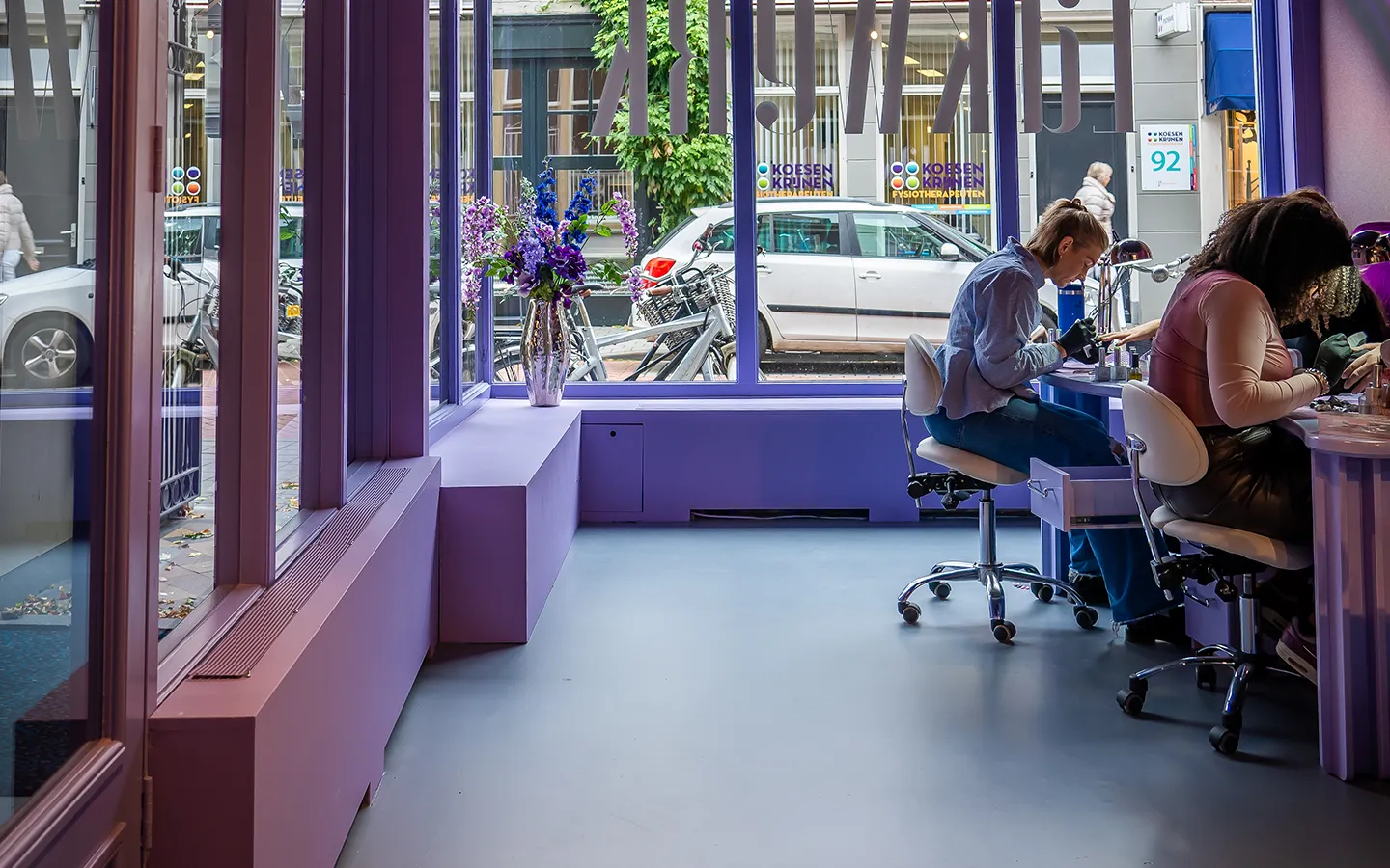 Interieur van nagelstudio Lakwerk in Amsterdam met paarse inrichting, grote raampartij en nagelstyliste aan het werk
