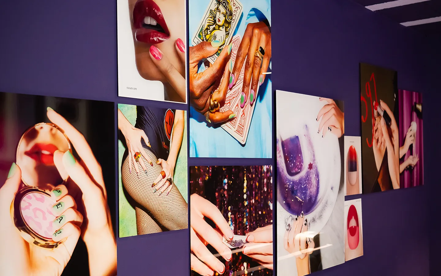 Inspiratiemuur van nagelstudio Lakwerk met kleurrijke nageldesign foto's op een paarse muur