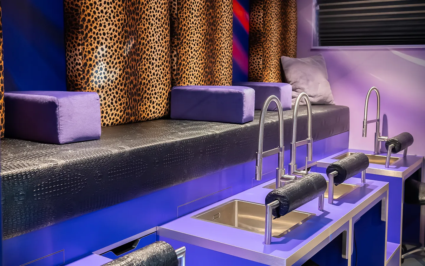 Pedicure werkplekken bij nagelstudio Lakwerk met paarse verlichting, gouden wastafels en luipaardprint gordijnen