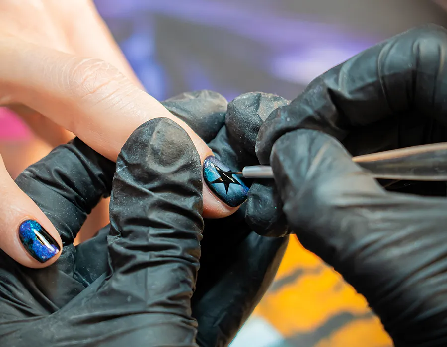 Close-up van nagelstyliste van Lakwerk die een ster nagelart aanbrengt op holografisch blauwe gelnagel