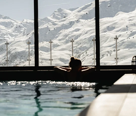 A woman enjoying the spa at the Ours Blanc hotel, looking out at the surrounding mountains from the pool and through the floor-to-ceiling windows