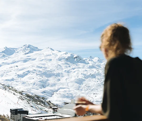 A woman looking out over the Les Menuires area on a sunny day from the balcony of a room at the Ours Blanc hotel