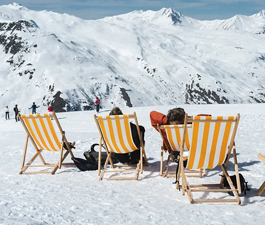 Holidaymakers on sun loungers at the edge of the slopes in the Les Menuires ski area, in front of the Ours Blanc hotel