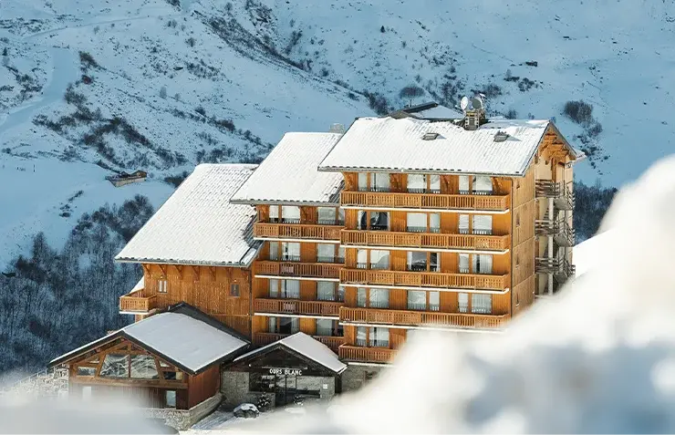 The snow-covered façade of the Ours Blanc hotel on a sunny day in Les Menuires during the winter season