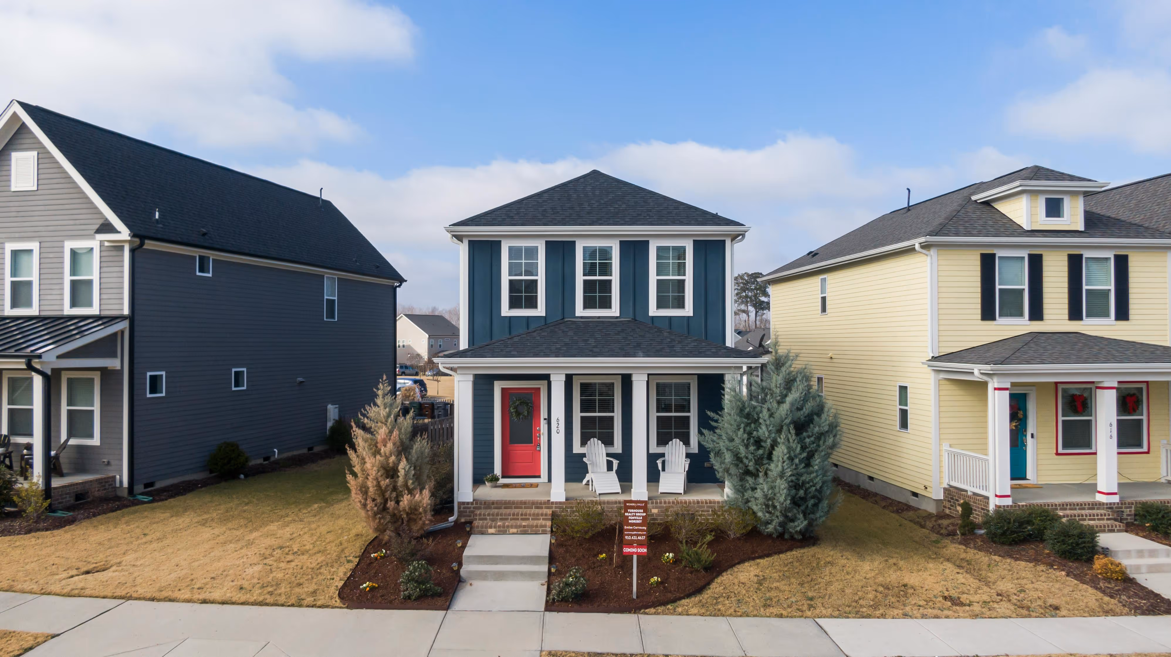 Newly built two-story home with dark blue-gray siding, white trim, and a red front door, flanked by neighboring houses on a residential street