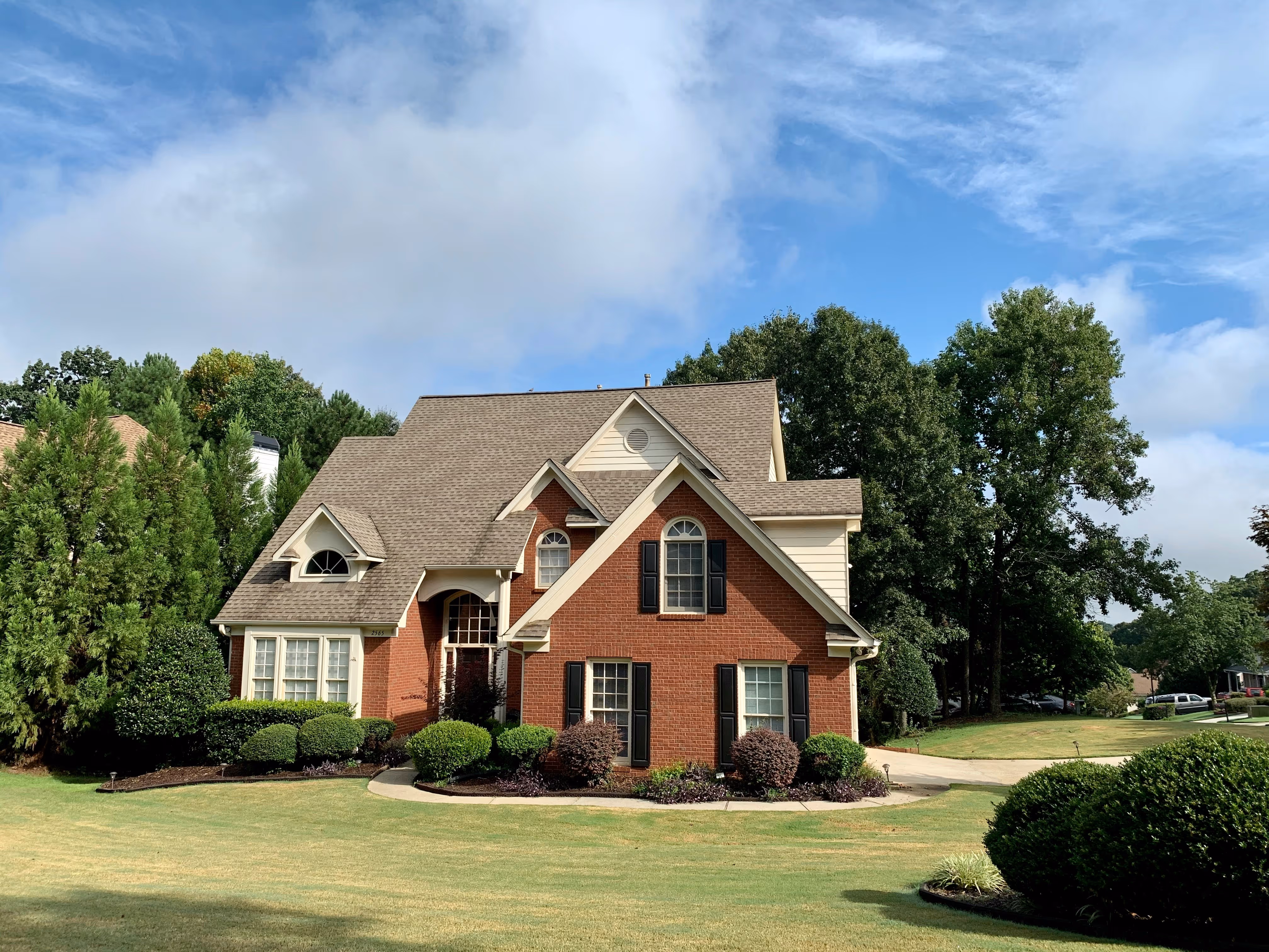Two-story brick home with dark shutters, covered entry porch, and landscaped front yard