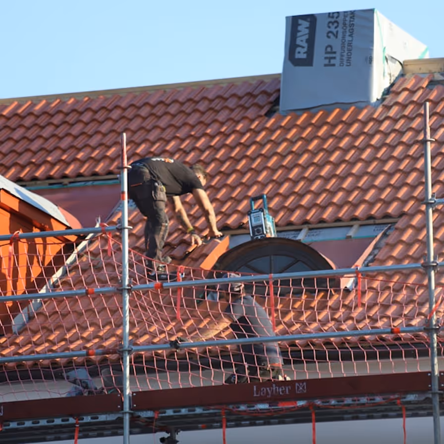 Roofer working on scaffolding while installing red clay tile roofing on a building