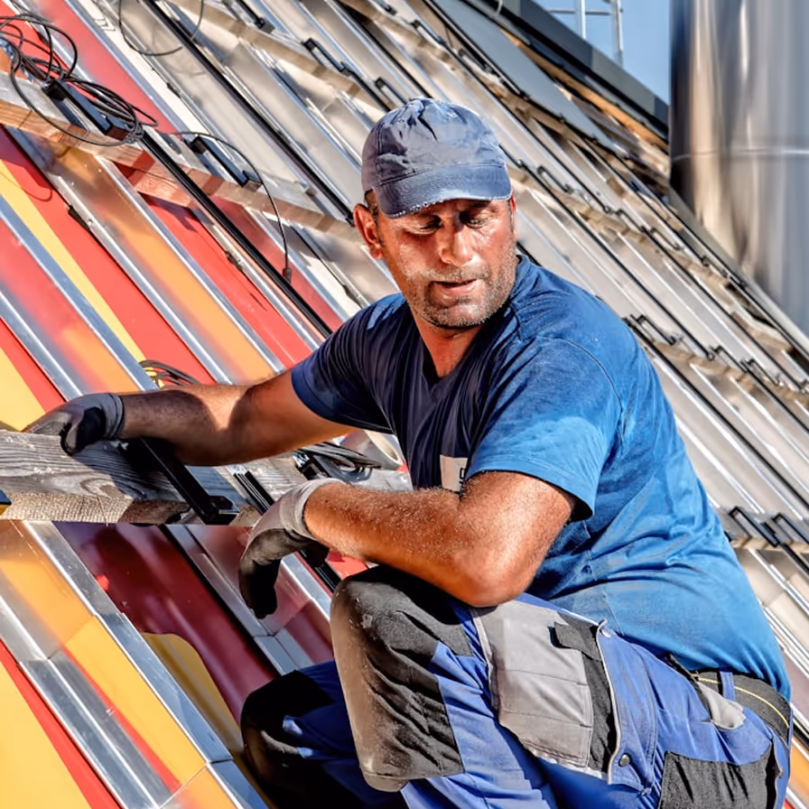 Roofing contractor kneeling on a metal panel roof installing colorful ribbed roofing sheets