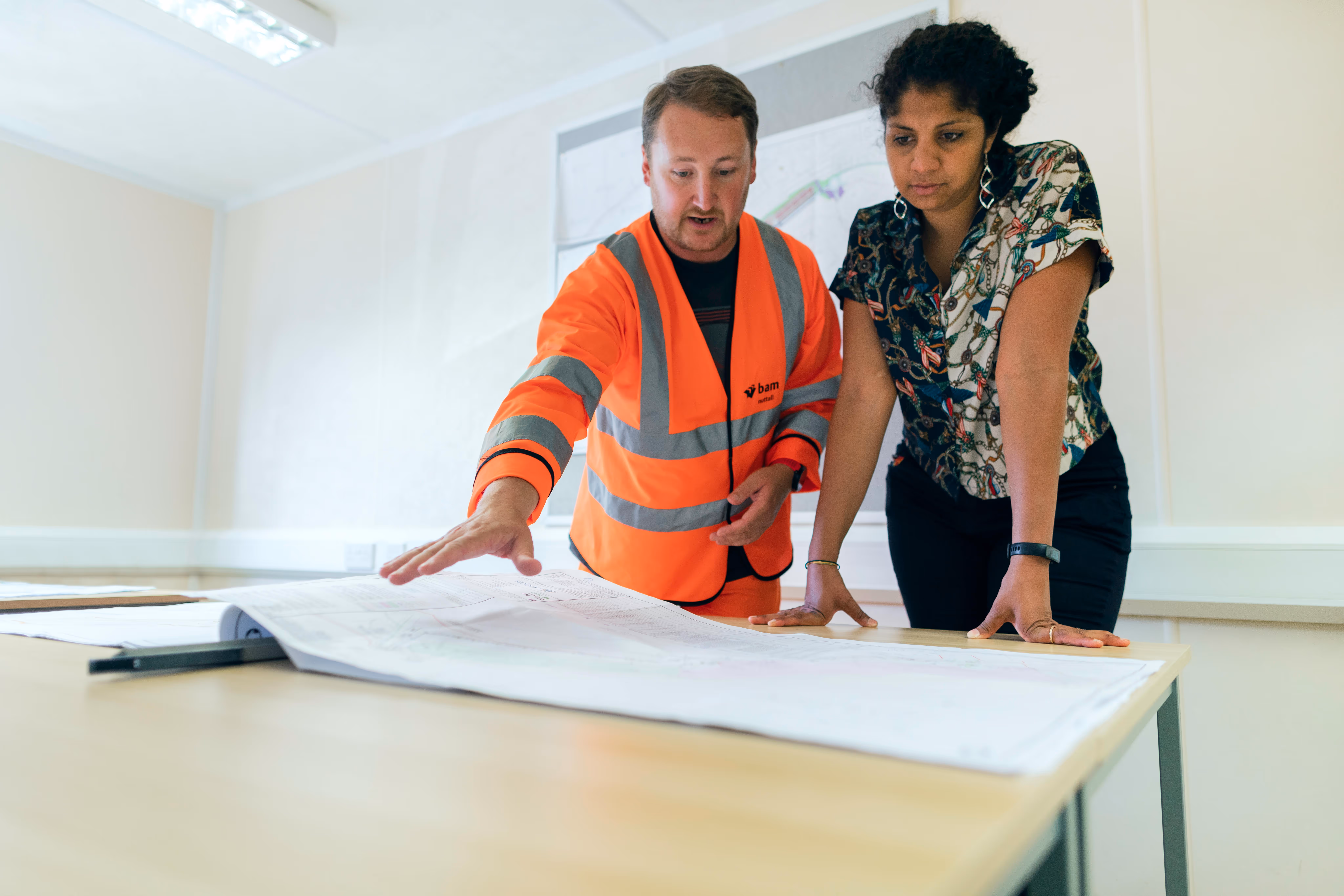 Contractor in an orange safety vest and a client reviewing blueprints spread out on a table