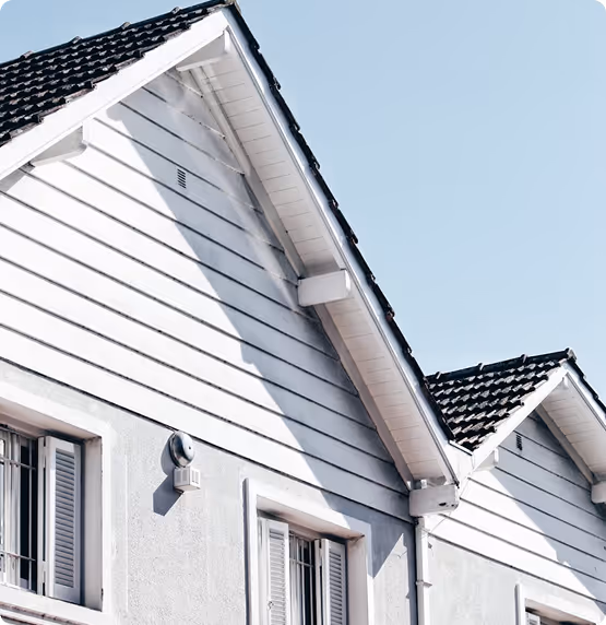 Close-up of white horizontal siding and matching gable trim on adjoining home roof peaks against a blue sky