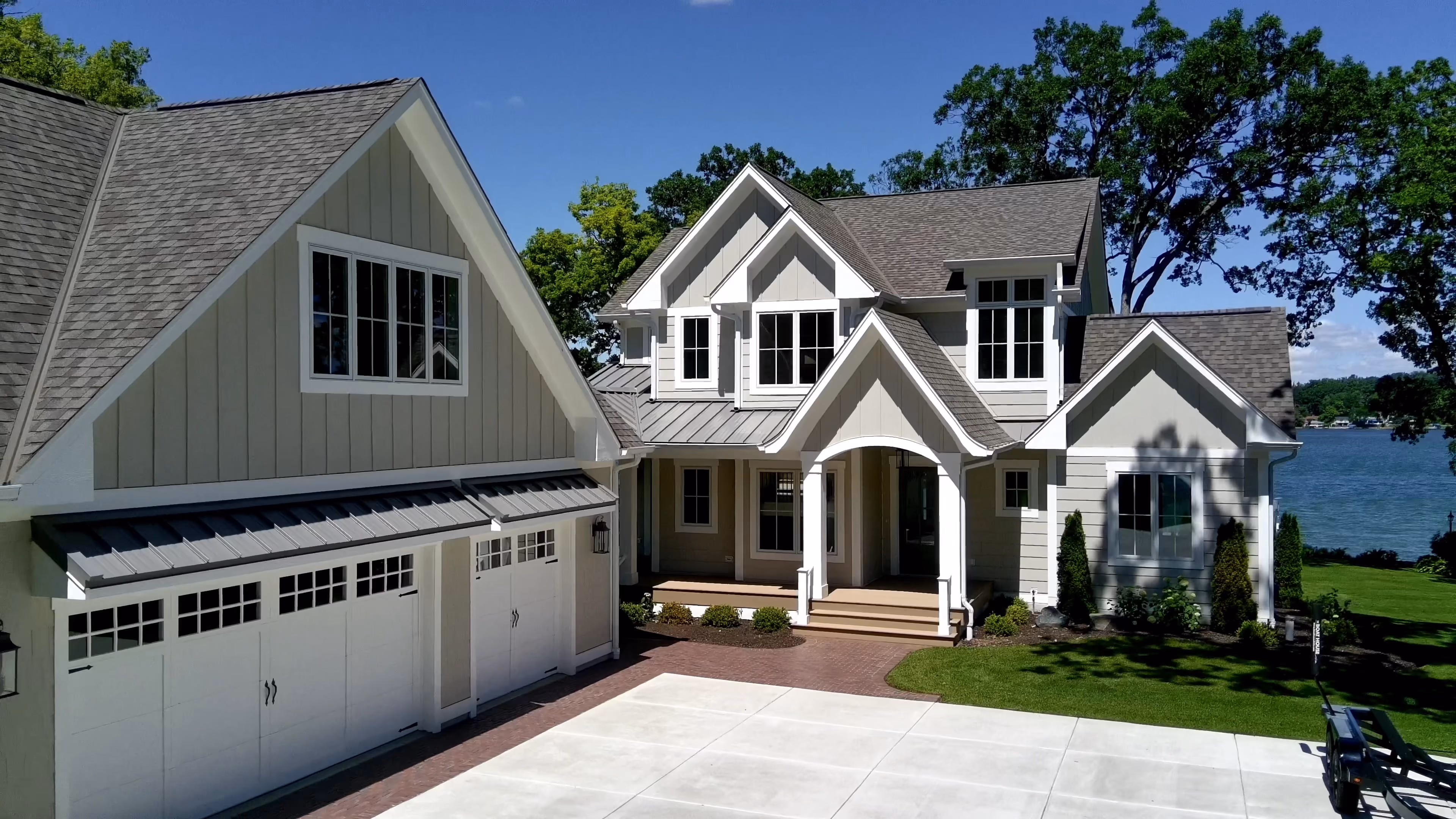 Two-story custom home with light siding, board-and-batten gable, and a two-car garage with carriage-style doors, overlooking a lake