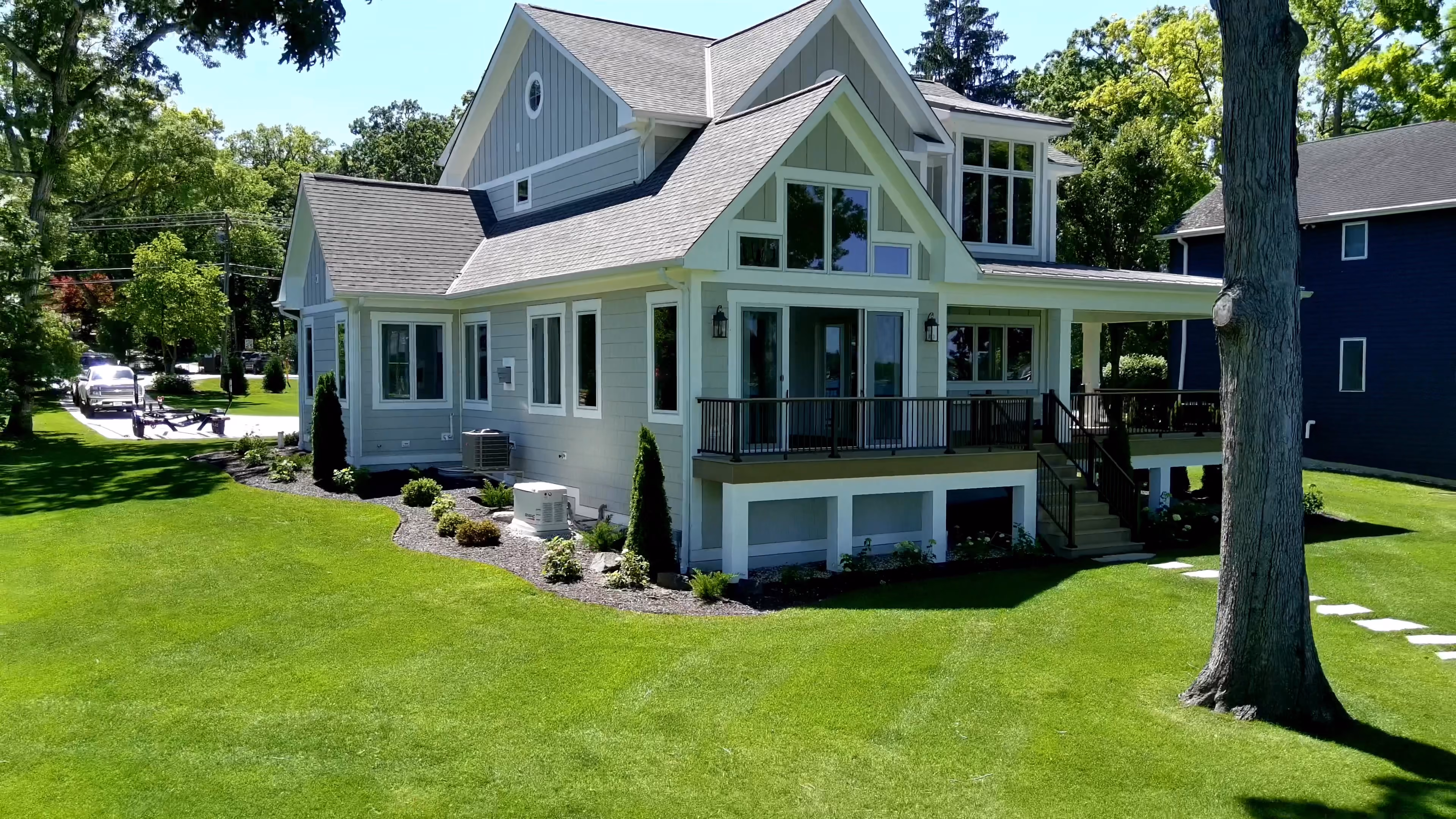 Finished two-story custom home with light siding and dark trim, covered deck, and a walkout lower level surrounded by mature lawn