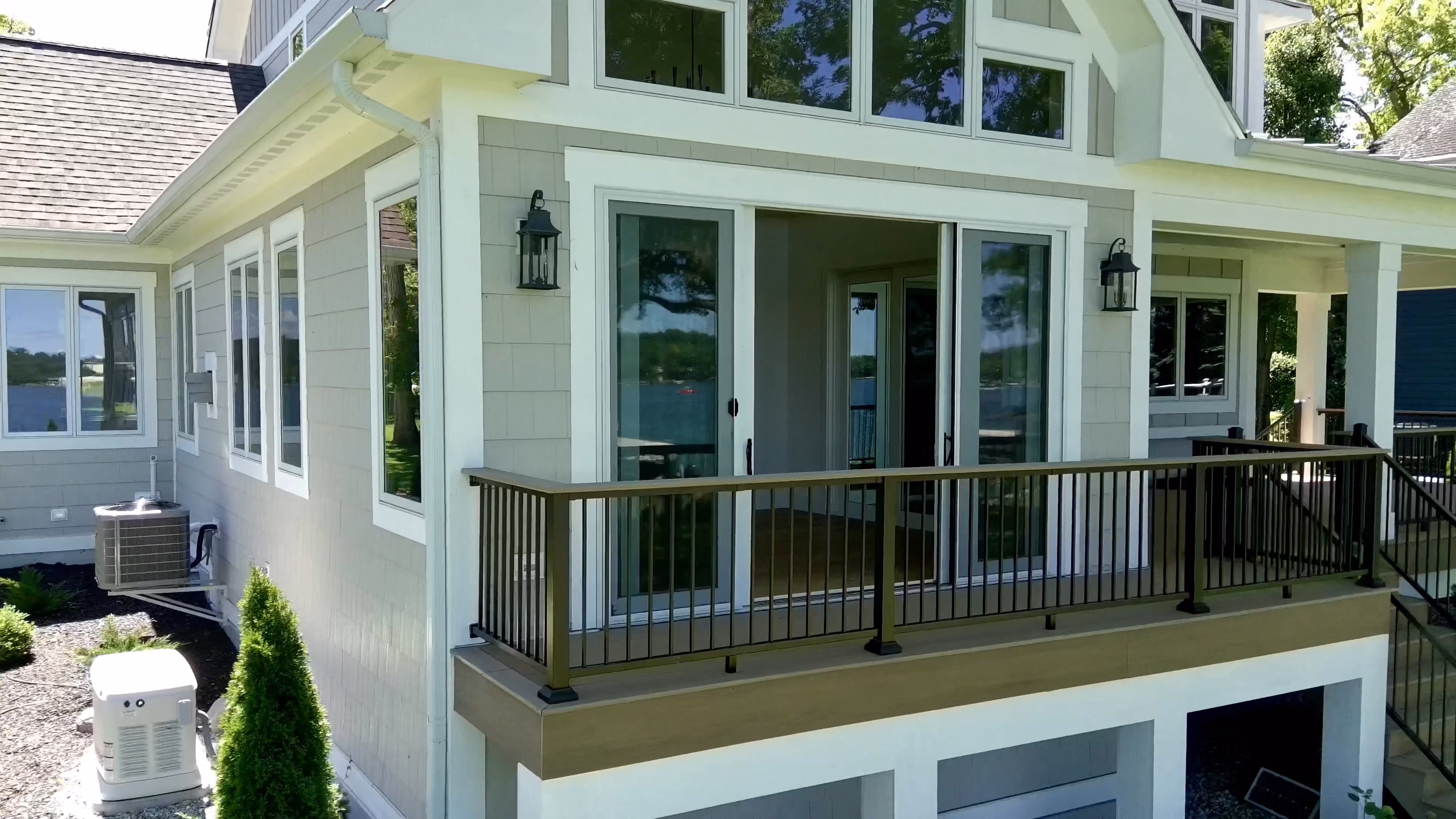 Close-up of a finished home's covered porch with sliding glass doors, wall sconce lighting, and a composite deck with black metal railing