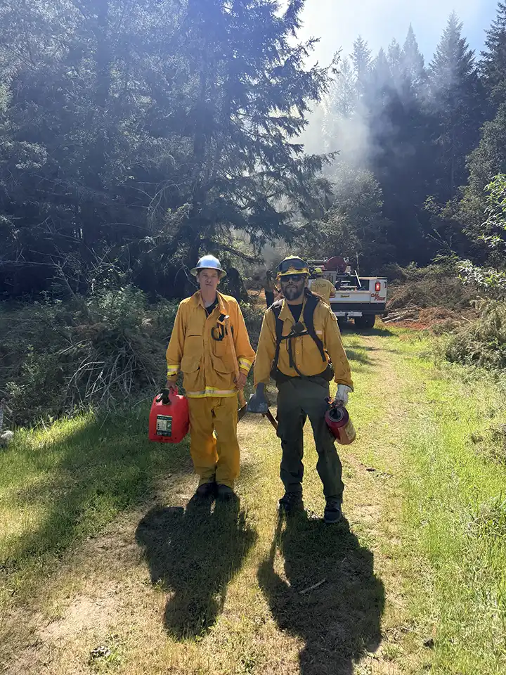Two workers carrying equipment along a forest track