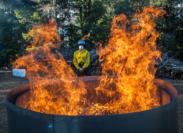 Worker monitoring flames inside a circular burn kiln