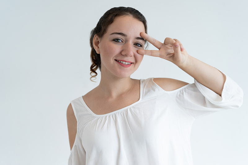 Smiling young woman making a peace sign beside her eye