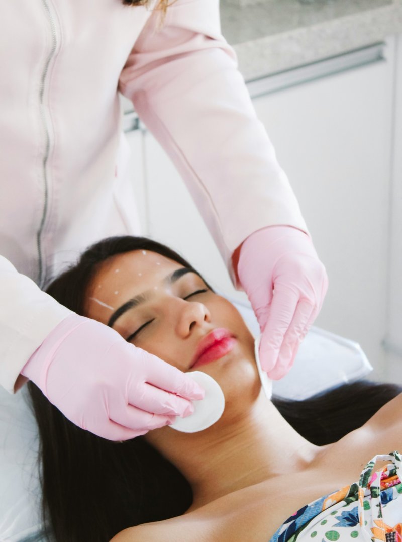 Therapist cleansing a woman's face with cotton pads during a facial