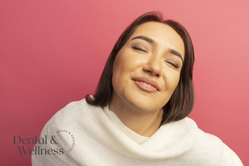 Smiling woman with her eyes closed against a pink background — lip flip